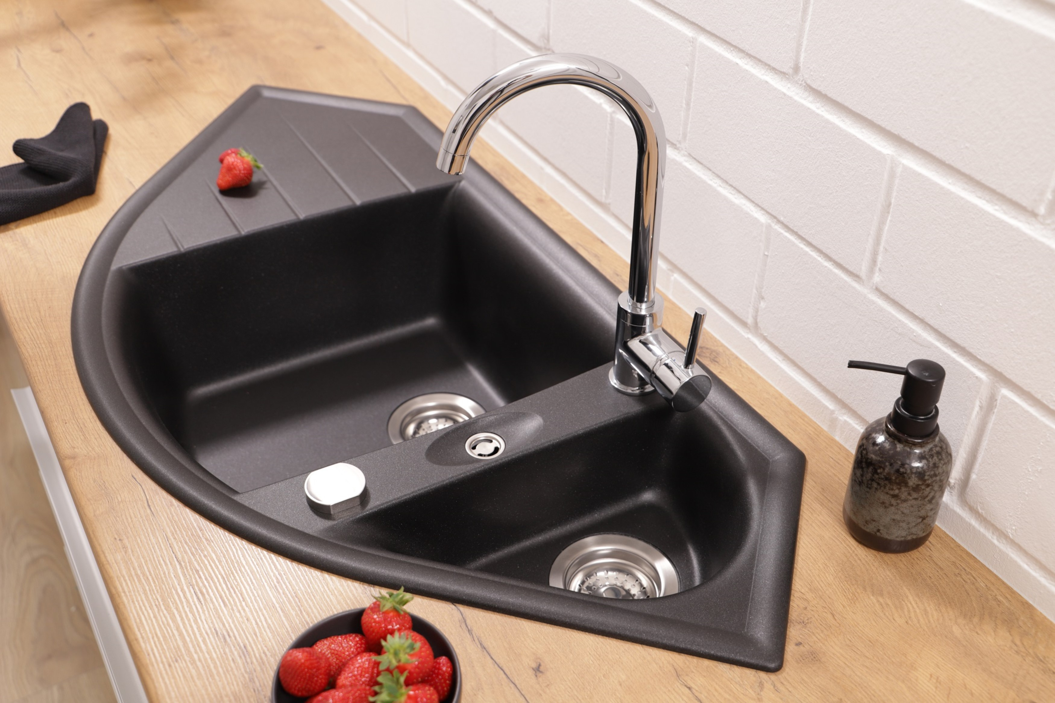 Schwarzes Küchenbecken mit Wasserhahn und Seifenspender, Erdbeeren und schwarze Handschuhe daneben.