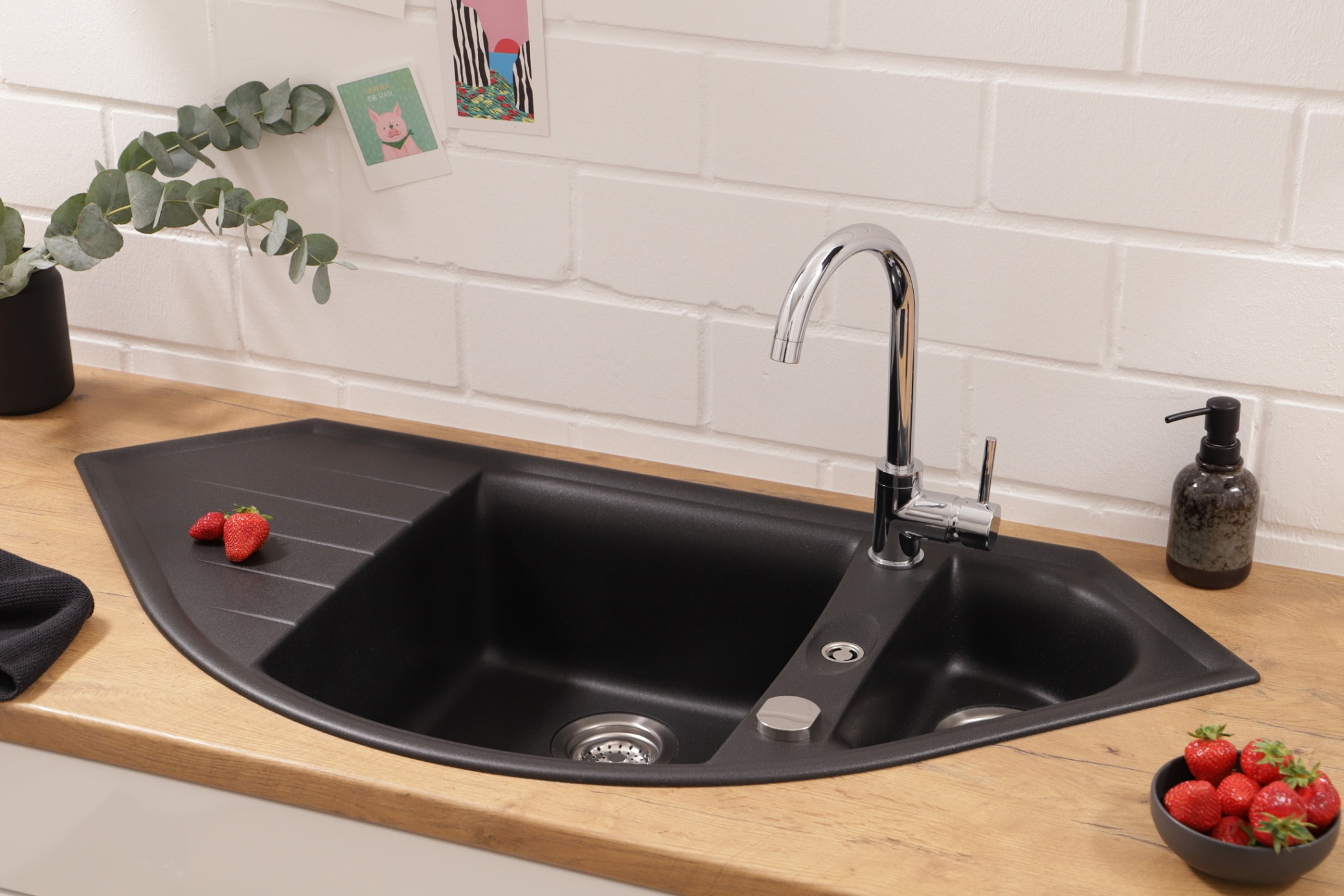 Schwarzes Küchenbecken mit Wasserhahn und Erdbeeren. Holz-Arbeitsplatte und weiße Ziegelwand.