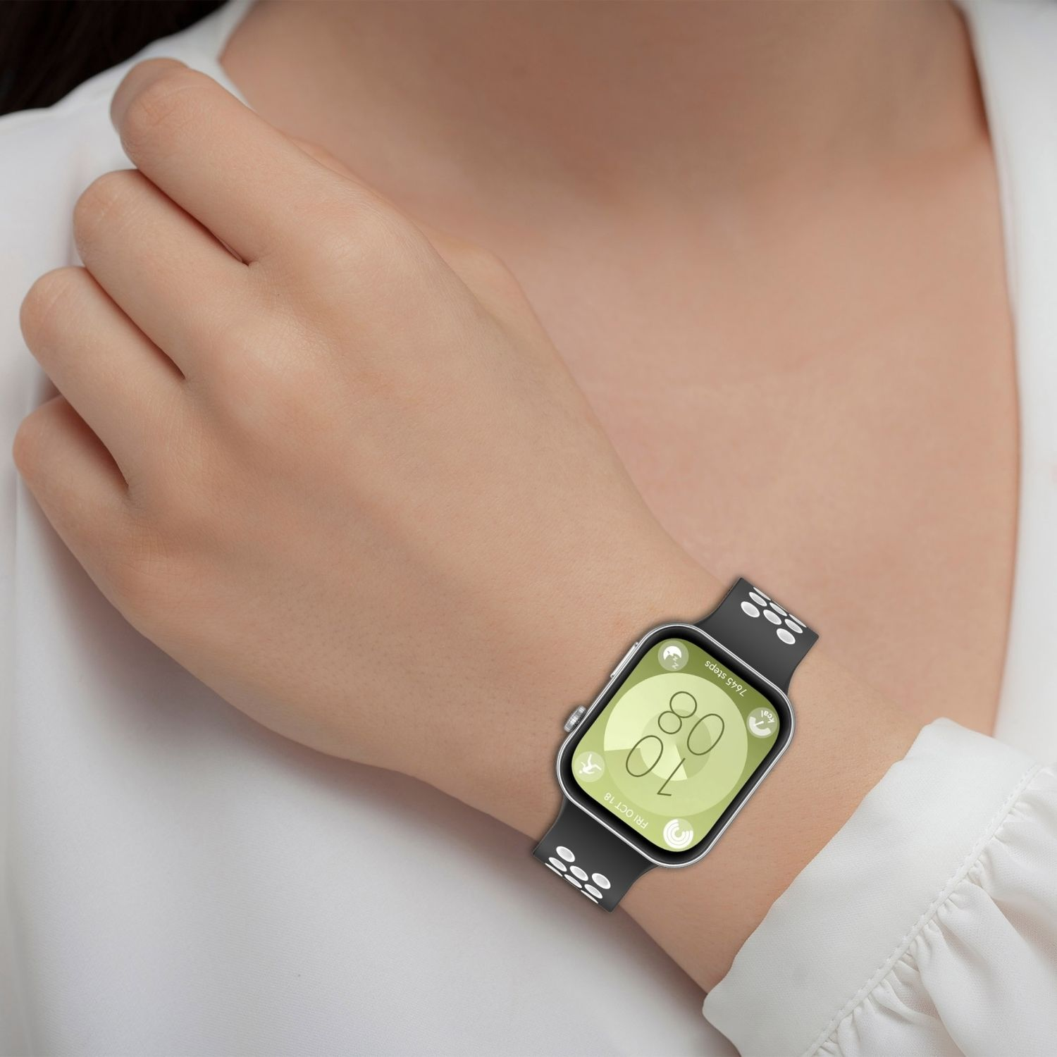 Das Handgelenk einer Frau mit einer schwarzen Uhr. Die Uhr zeigt Datum und Uhrzeit an. Das Band ist schwarz mit weißen Punkten.