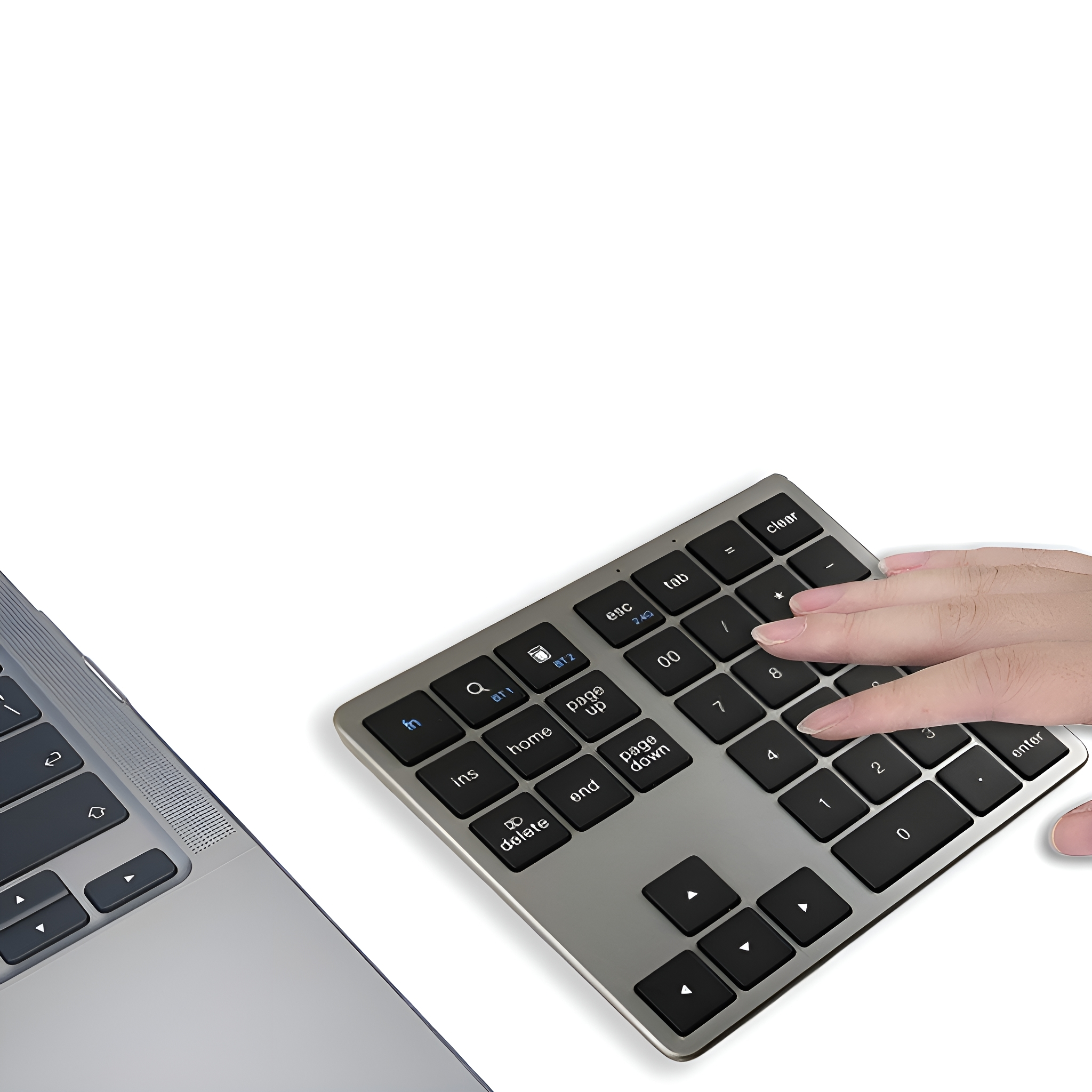 Eine Hand benutzt einen silbernen Nummernblock neben einem Laptop, beides auf einer weißen Oberfläche.