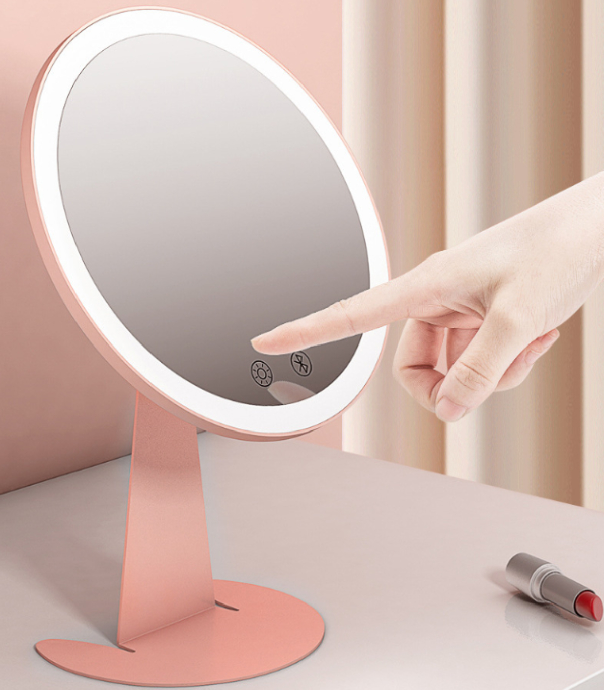 Ein rosa Schminkspiegel, ein Finger berührt den Bildschirm. Ein Lippenstift liegt auf dem Tisch.