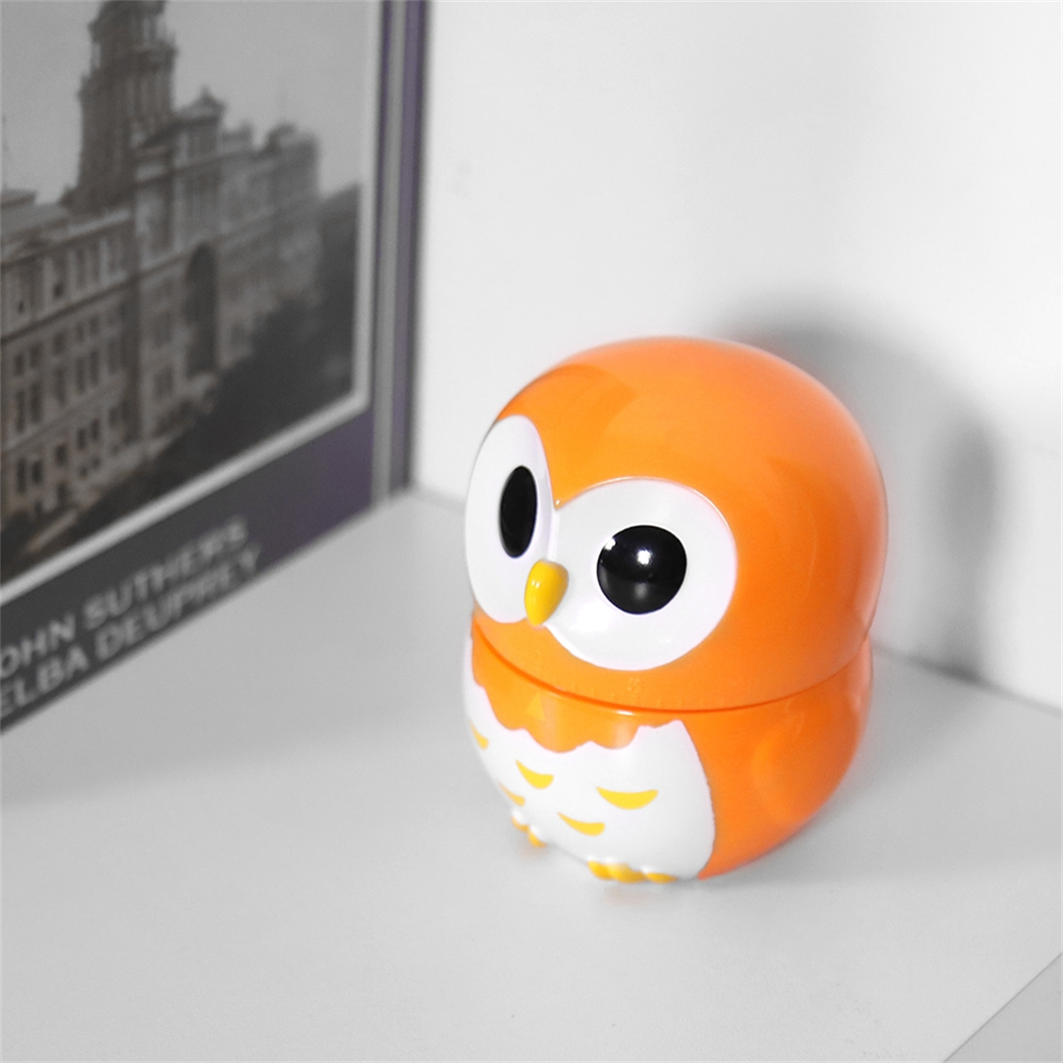 Ein orangefarbener eulenformiger Behälter auf einer weißen Oberfläche mit verschwommenem Hintergrund.