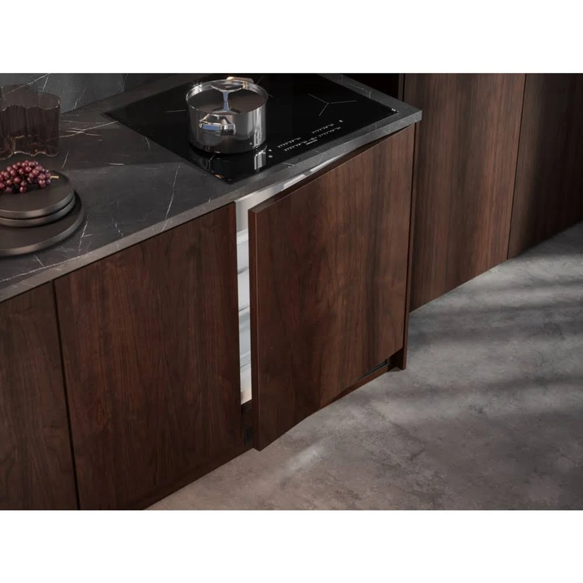 Una cucina con mobili in legno scuro, un piano cottura a induzione e un cassetto del frigorifero parzialmente aperto con luce all'interno.