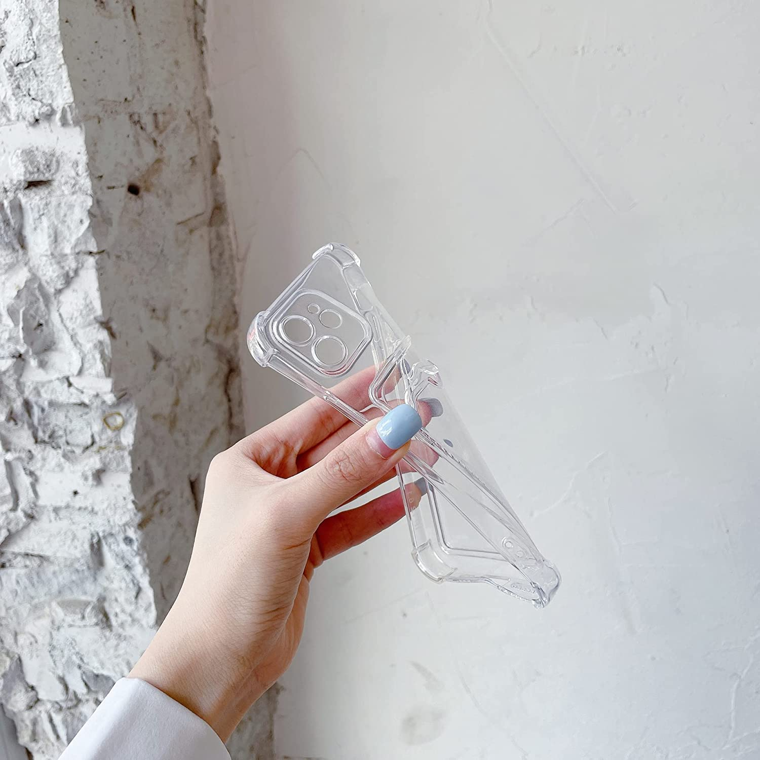Eine Hand hält eine transparente Handyhülle vor einem weißen Backsteinmauer-Hintergrund.