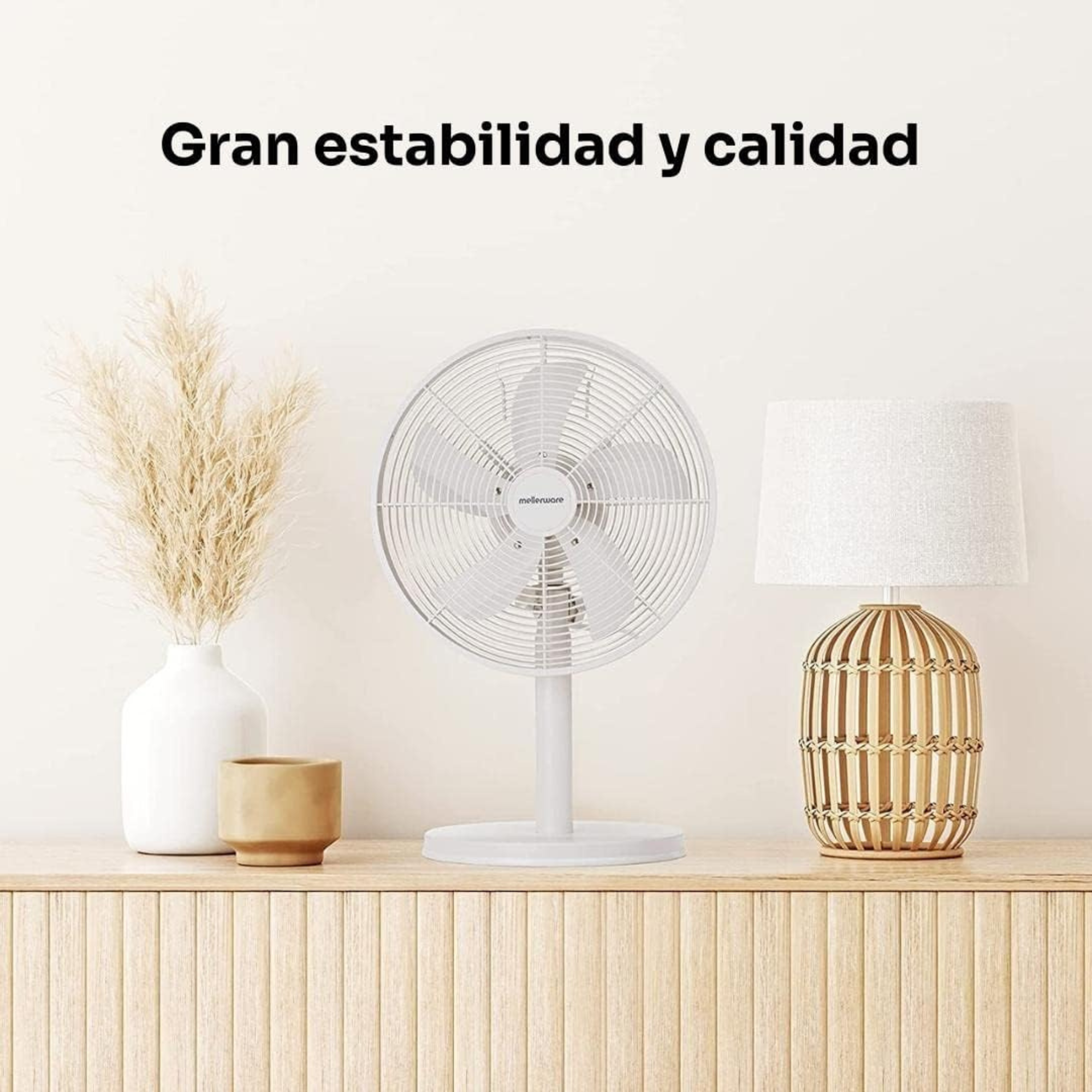 Ventilatore bianco su un mobile in legno con oggetti decorativi. Una lampada e un vaso sono accanto al ventilatore.