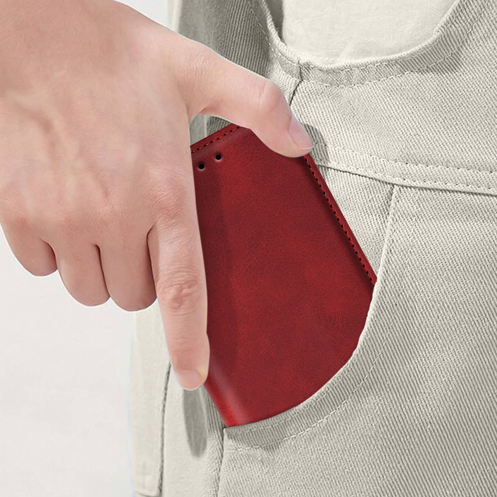 Una mano che tiene una custodia per telefono rossa nella tasca di pantaloni beige. La custodia è parzialmente visibile.