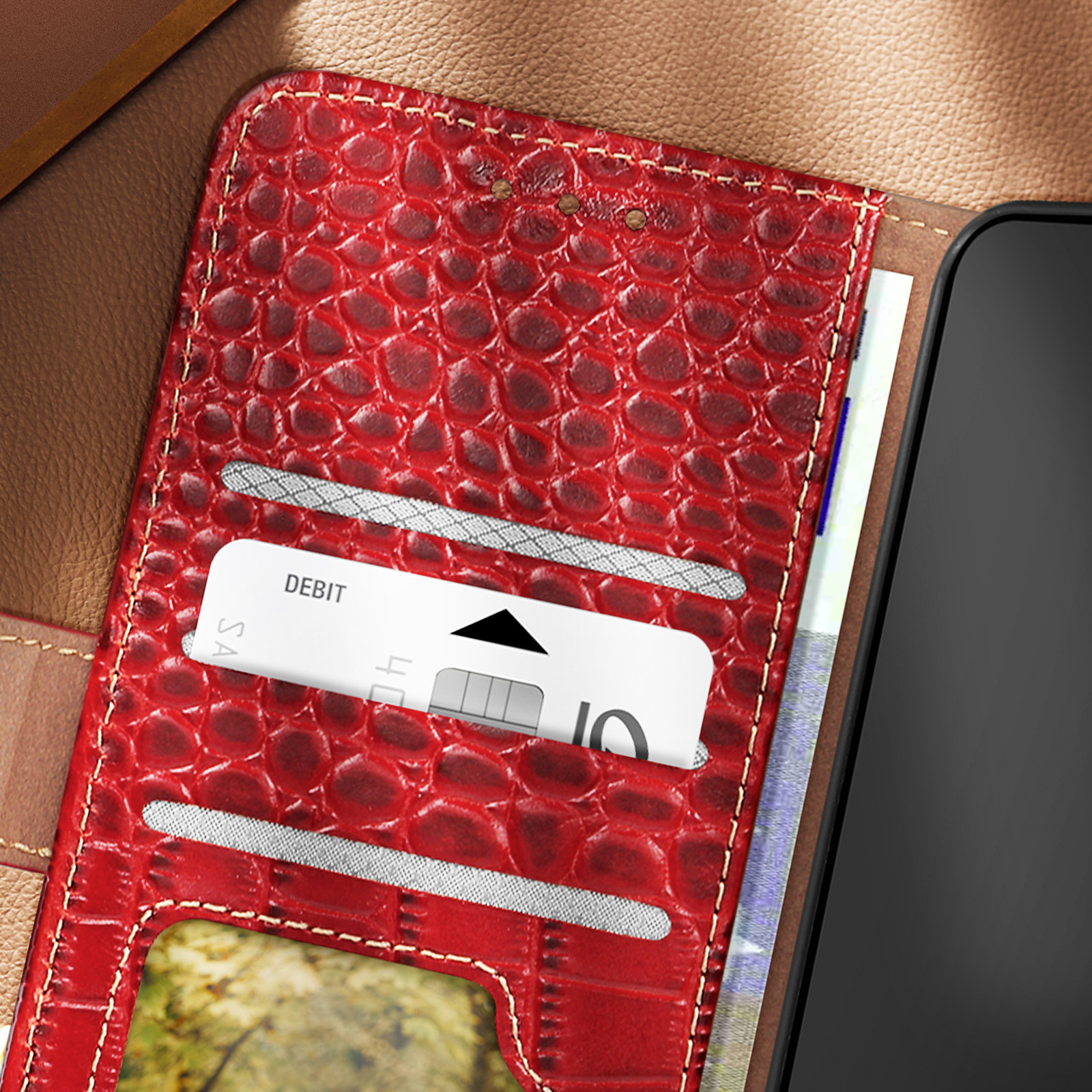 Custodia per telefono in pelle rossa con scomparti per carte, con carta di debito e denaro su superficie marrone.