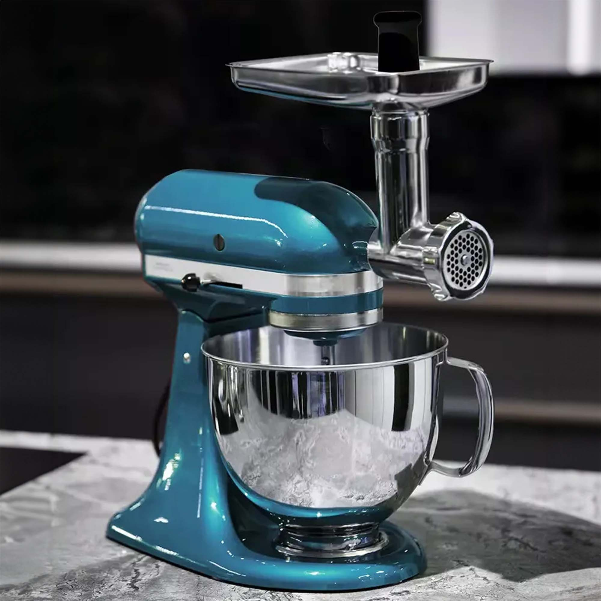 Ein türkisfarbener Küchenmixer mit Fleischwolfaufsatz. Eine silberne Schüssel darunter, auf Marmor.