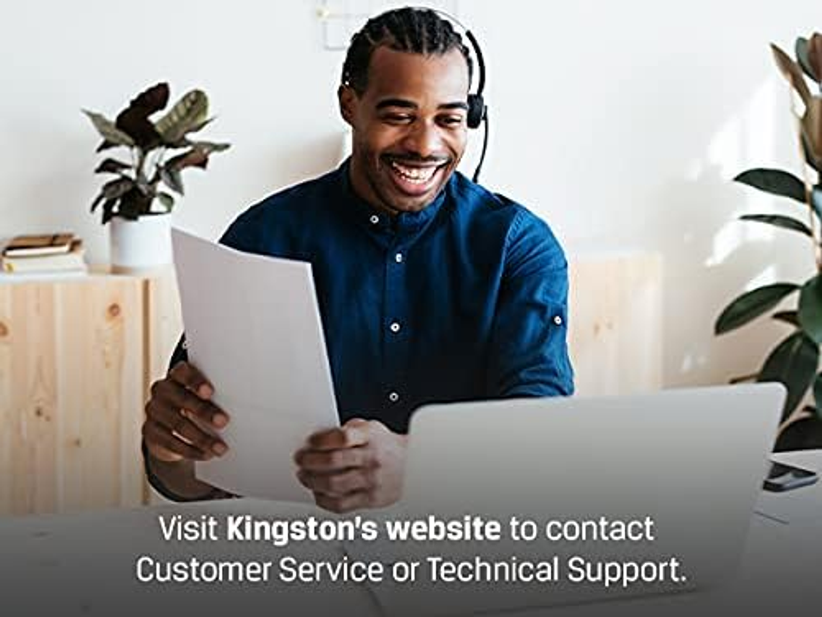 Mężczyzna z zestawem słuchawkowym uśmiecha się i trzyma papiery, obok laptopa. Tekst: Odwiedź stronę internetową Kingston.