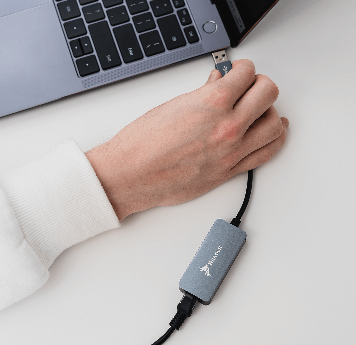 Ręka osoby podłączająca kabel USB do laptopa. Szary adapter jest podłączony do kabla.