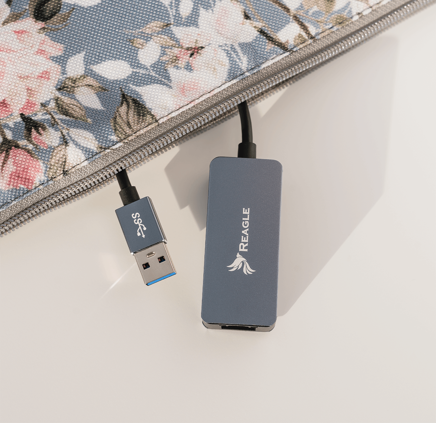 Niebieski hub USB i kabel obok etui we wzór kwiatowy. Białe tło.