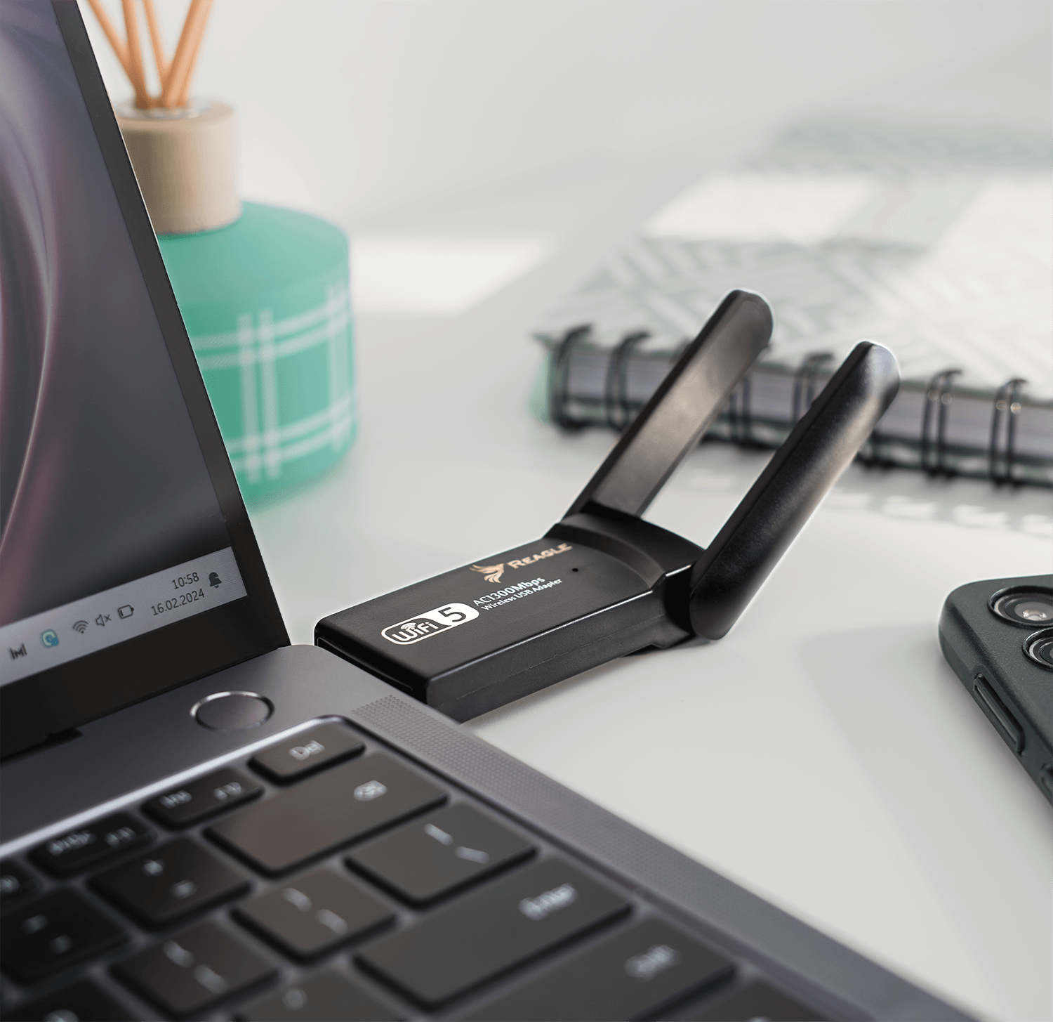 Laptop z podłączonym adapterem WiFi, obok telefonu i notatnika.