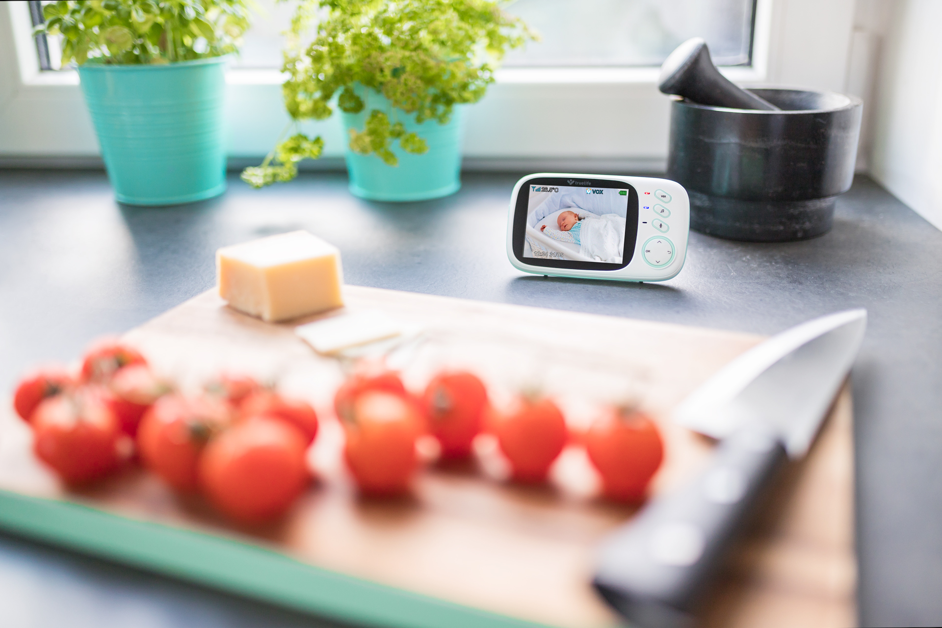 Babyphone mit Baby, Tomaten und Käse auf einem Brett.