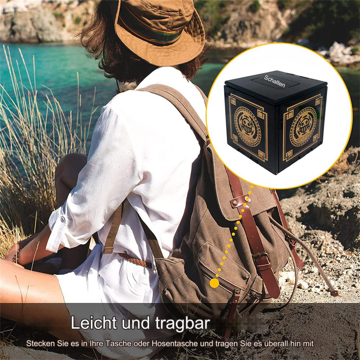 Eine Person am Meer mit einem Rucksack und einer schwarzen Box. Die Box hat ein Design auf der Vorderseite.