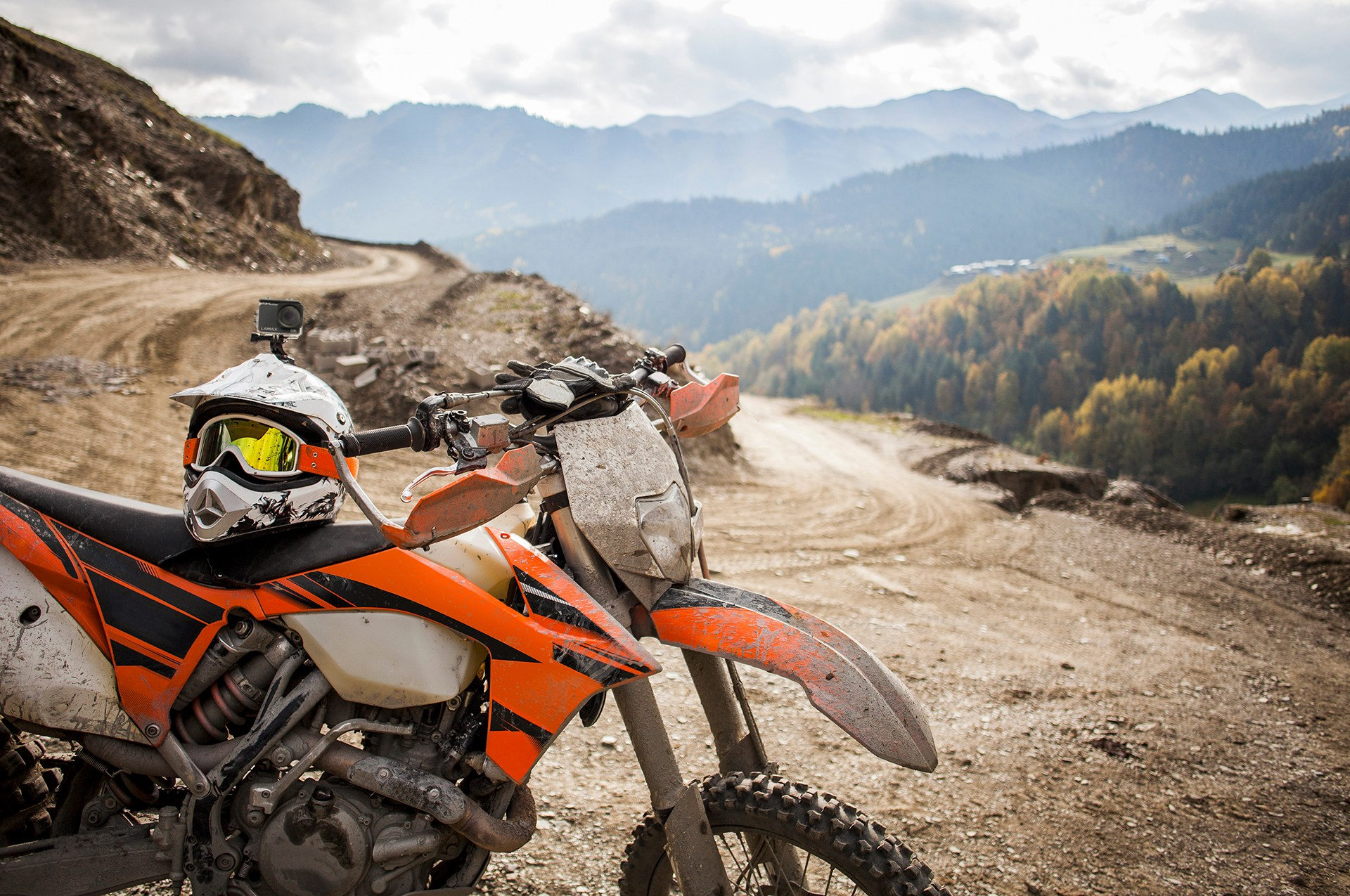 Motocross-Motorrad auf einer Schotterstraße mit Bergen im Hintergrund. Helm auf dem Motorrad.