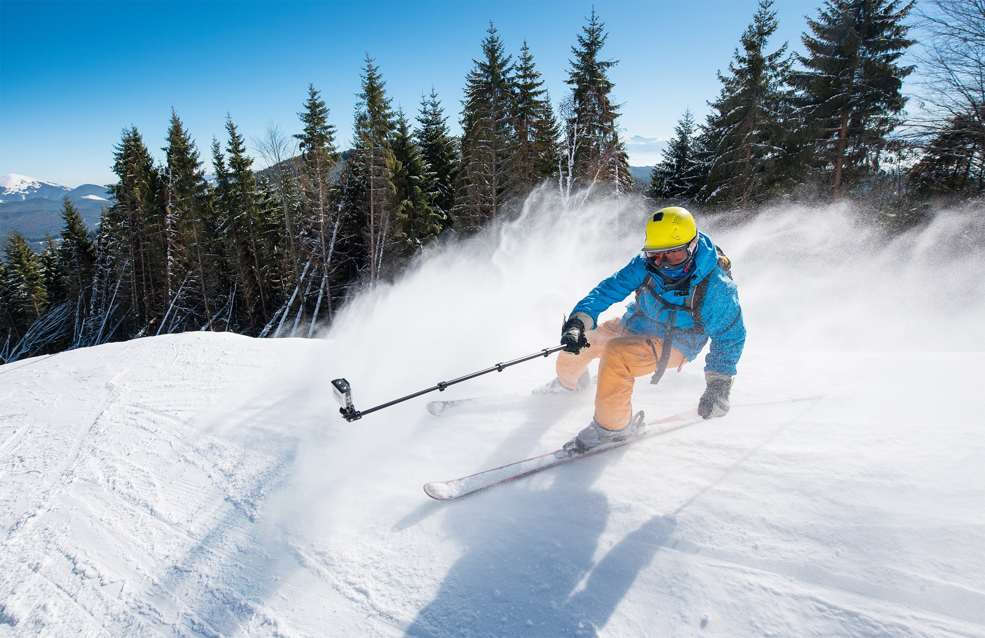 Skifahrer in blauer und gelber Ausrüstung fährt bergab und erzeugt eine Schneewolke.