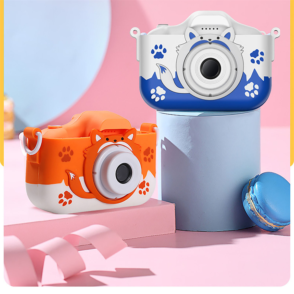 Zwei Spielzeugkameras: orange und blau, auf rosa und blauer Fläche.