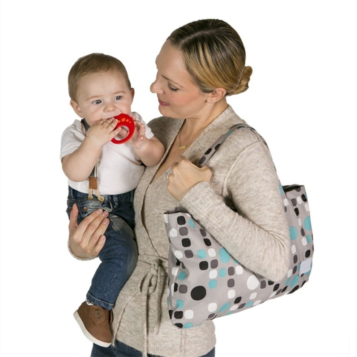 Eine Frau hält ein Baby, gibt ihm einen Beißring, mit einer gepunkteten Tasche. Sie sind in einem Zuhause.