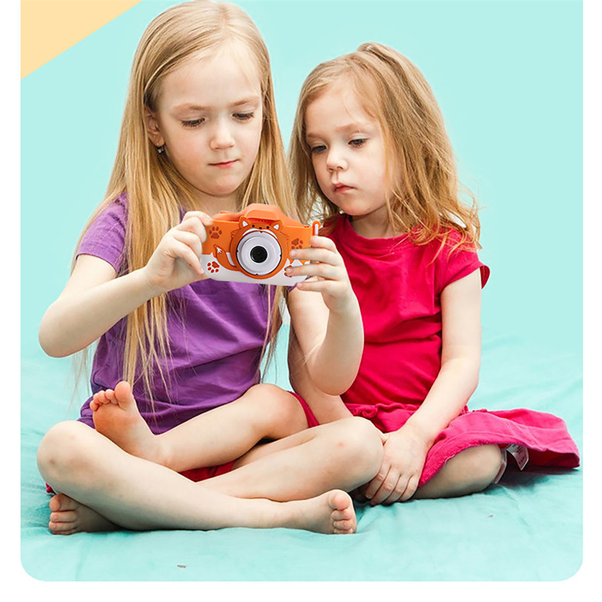 Zwei junge Mädchen betrachten eine orangefarbene Spielzeugkamera mit weiß-orangefarbenem Design, auf einem Schoß.