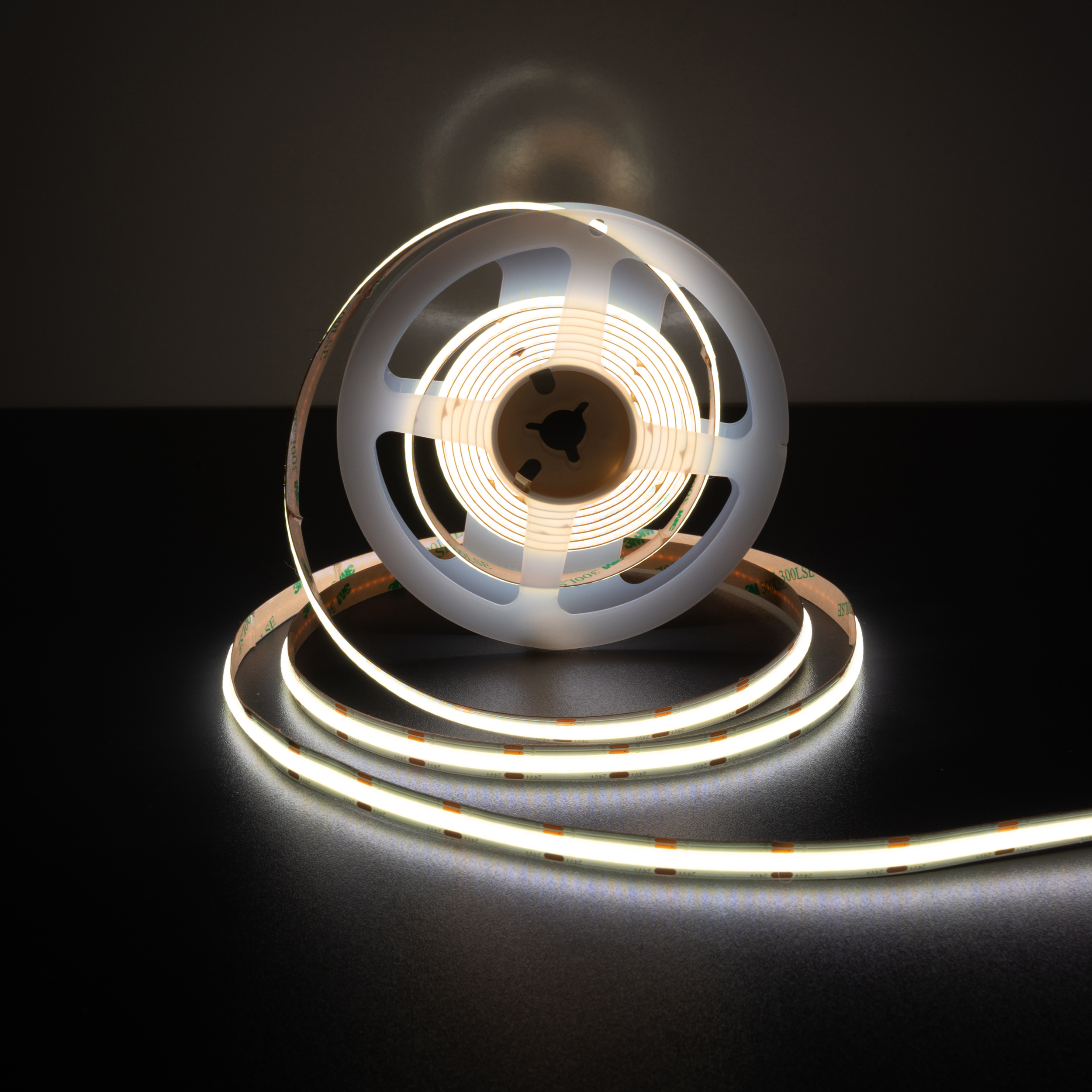 Rolle weißer LED-Lichtstreifen mit einer transparenten Kunststoffspule auf schwarzem Untergrund, die Licht aussendet.
