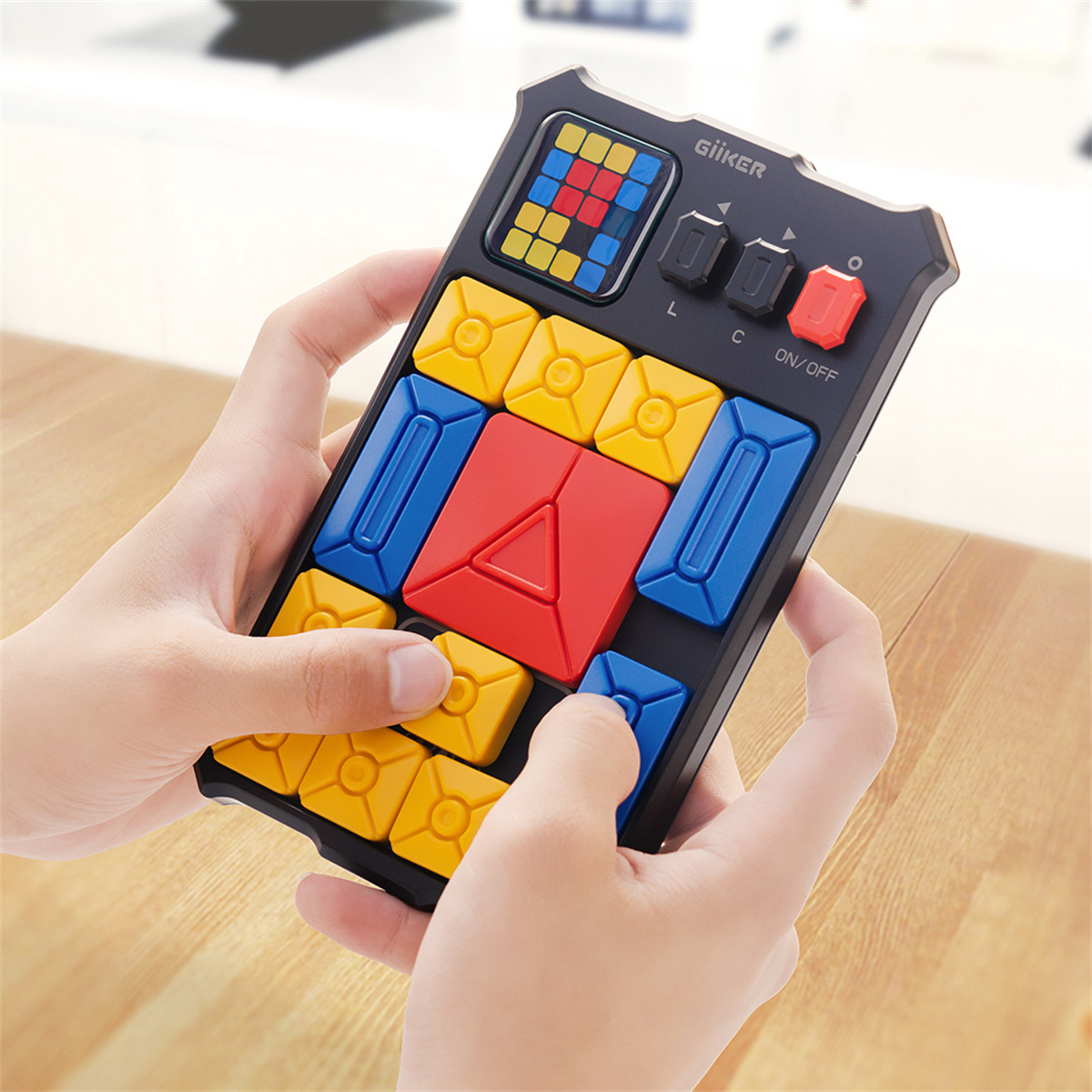 Hände halten ein schwarzes Puzzlespiel mit bunten Blöcken. Gelbe, blaue und rote Blöcke sind sichtbar. Das Spiel ist AN.