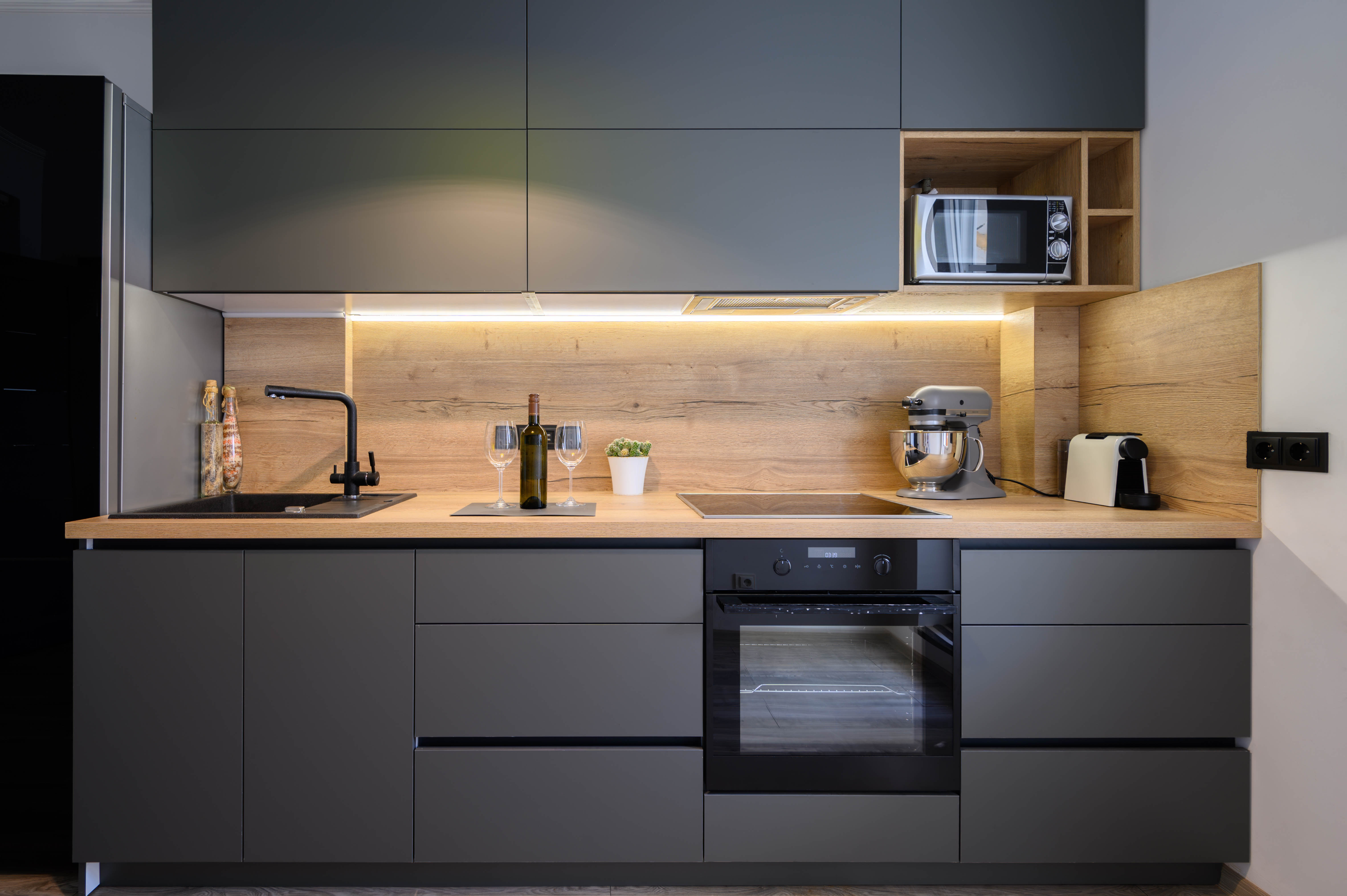 Moderne Küche mit grauen Schränken, Holz-Arbeitsplatte und Einbaugeräten. Enthält eine Mikrowelle, einen Ofen und ein Waschbecken.