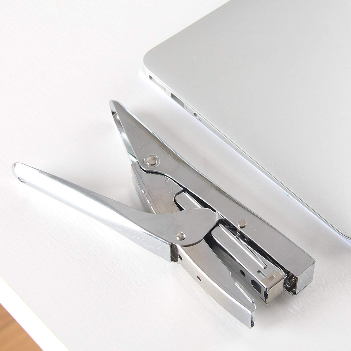 Silberner Tacker und Laptop auf weißer Oberfläche. Tacker ist offen, Laptop ist geschlossen.