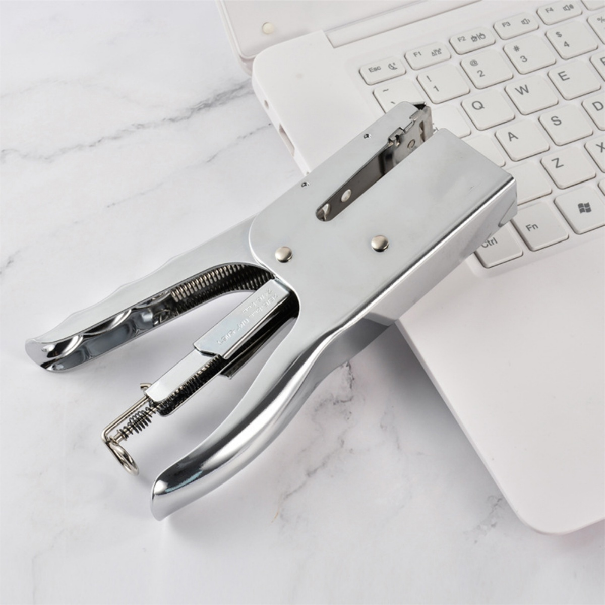 Silberner Tacker auf weißer Laptop-Tastatur. Der Tacker ist offen.
