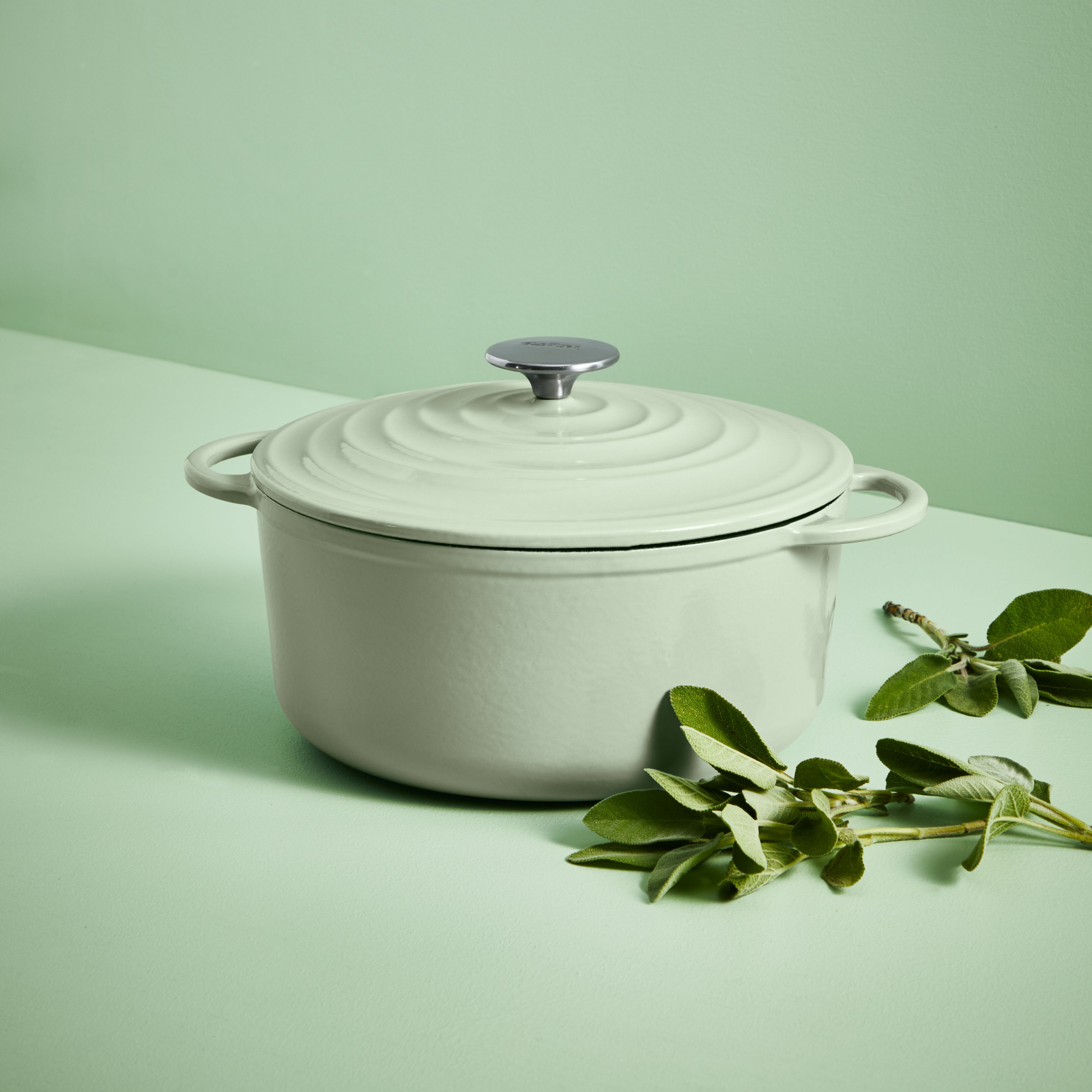 Jasnozielony garnek z pokrywką. Liście szałwii obok niego na zielonej powierzchni.