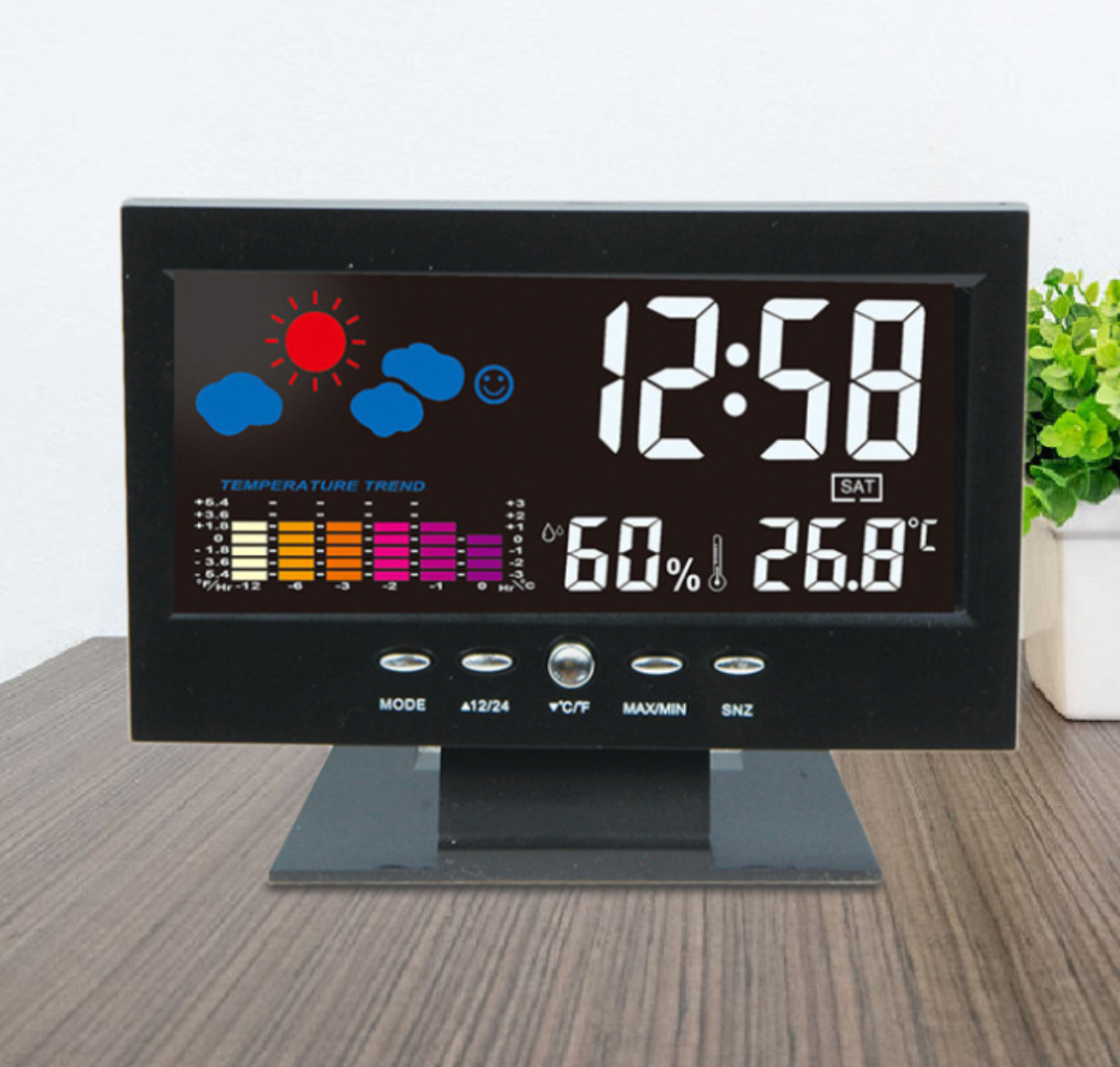 Schwarze Digitaluhr mit Wettersymbolen, Zeit, Temperatur und Luftfeuchtigkeit auf einem Holztisch.