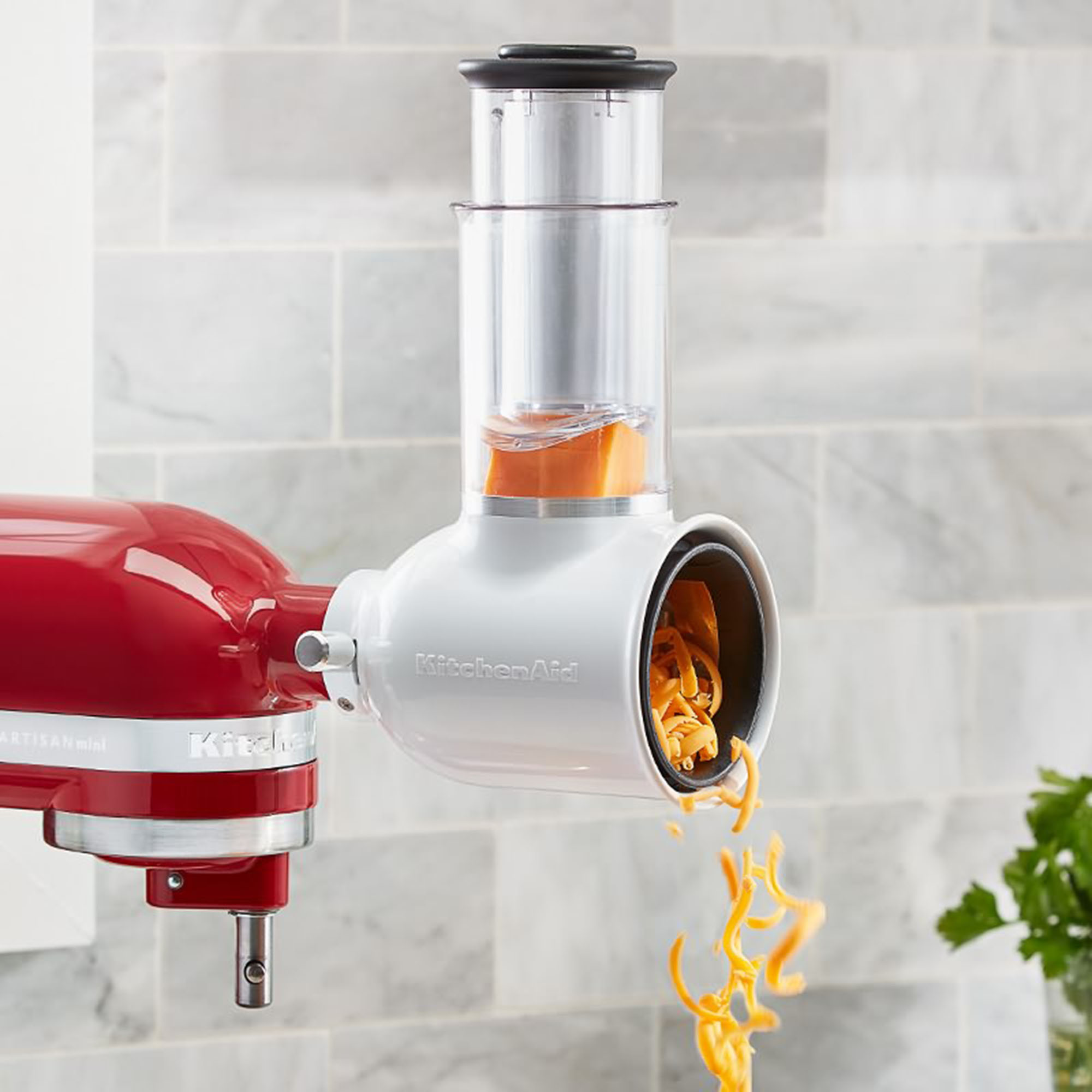 Ein roter KitchenAid-Mixer mit einem weißen Aufsatz für die Küchenmaschine, der Käse raspelt.