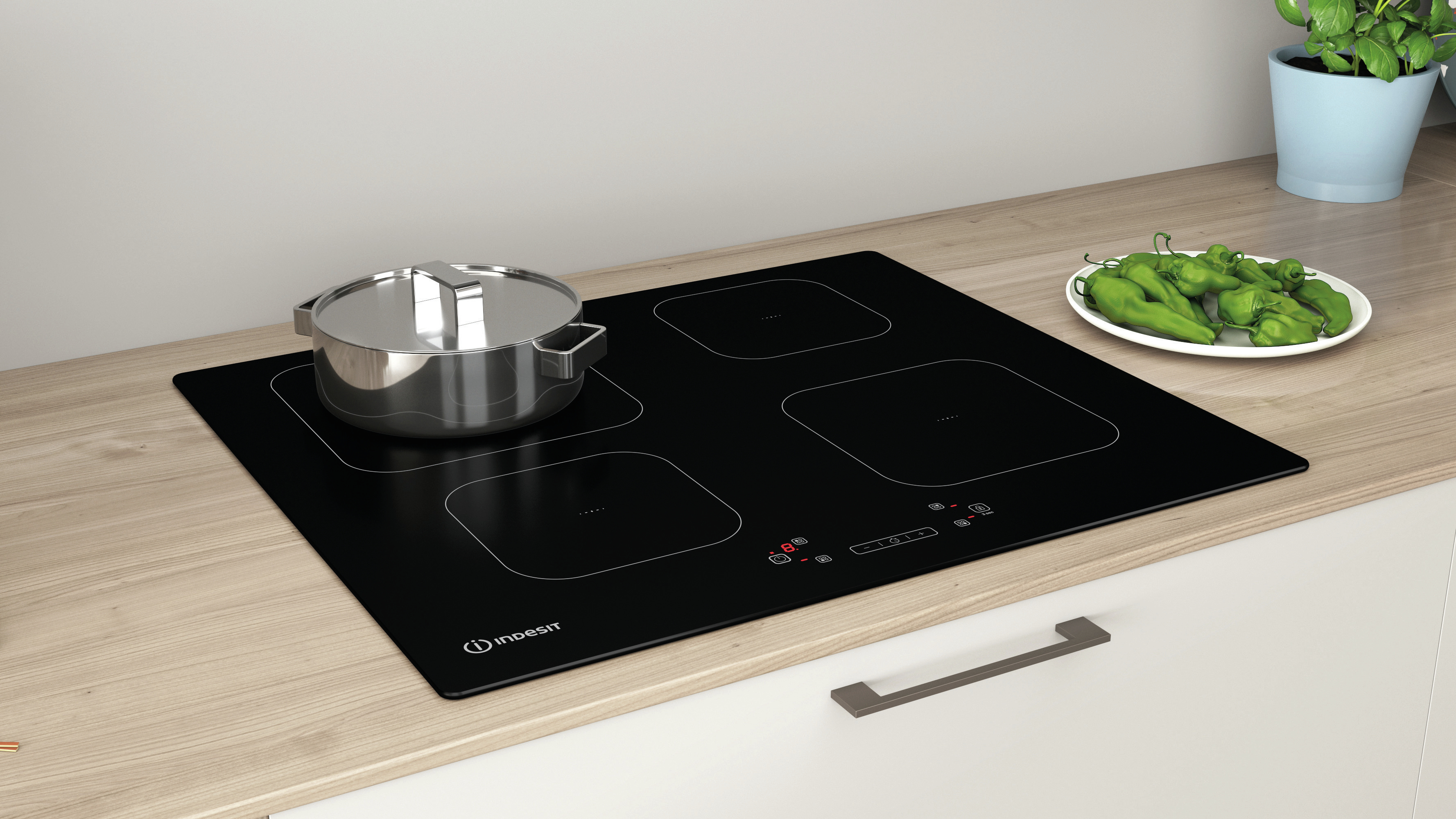 Czarna płyta indukcyjna z czterema strefami grzewczymi. Garnek i papryka na drewnie.