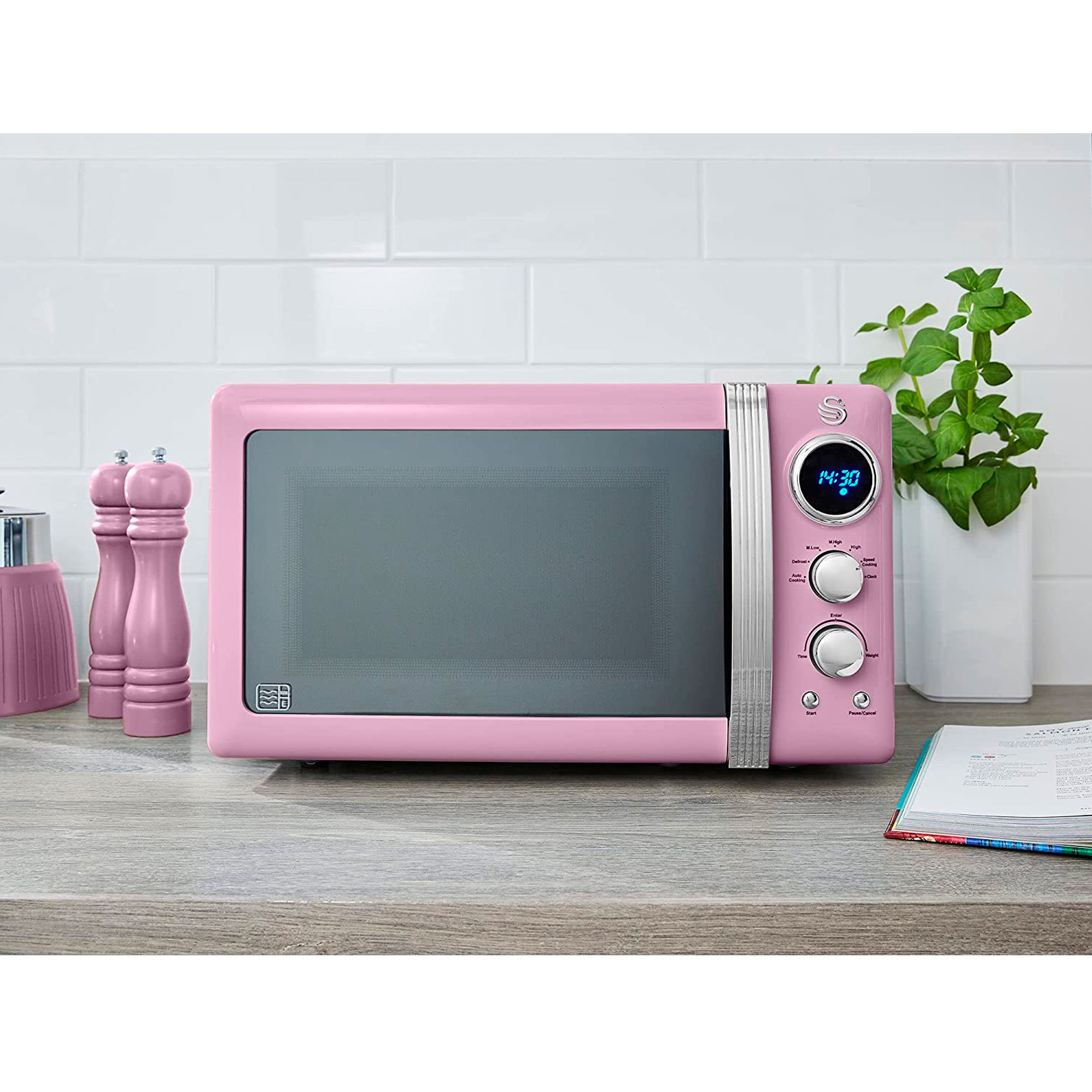 Un horno microondas rosa sobre una encimera de madera con fondo de azulejos blancos.