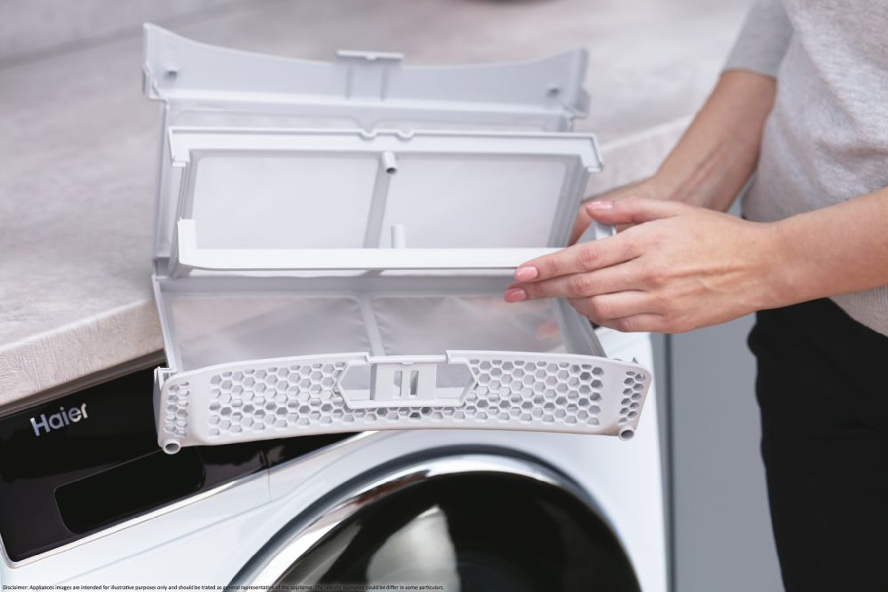 Ręce osoby wyjmującej filtr z białej suszarki. Widoczna marka Haier.