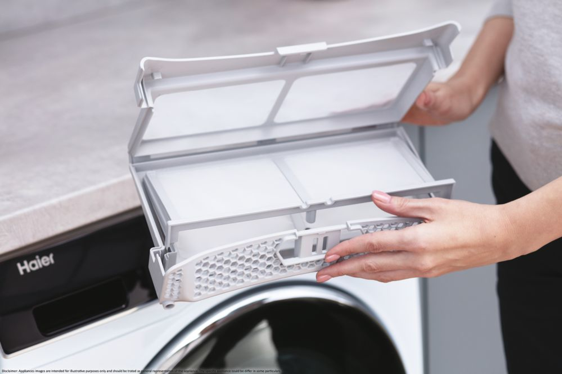 Ręce osoby wyjmujące filtry z szarego bębna pralki.