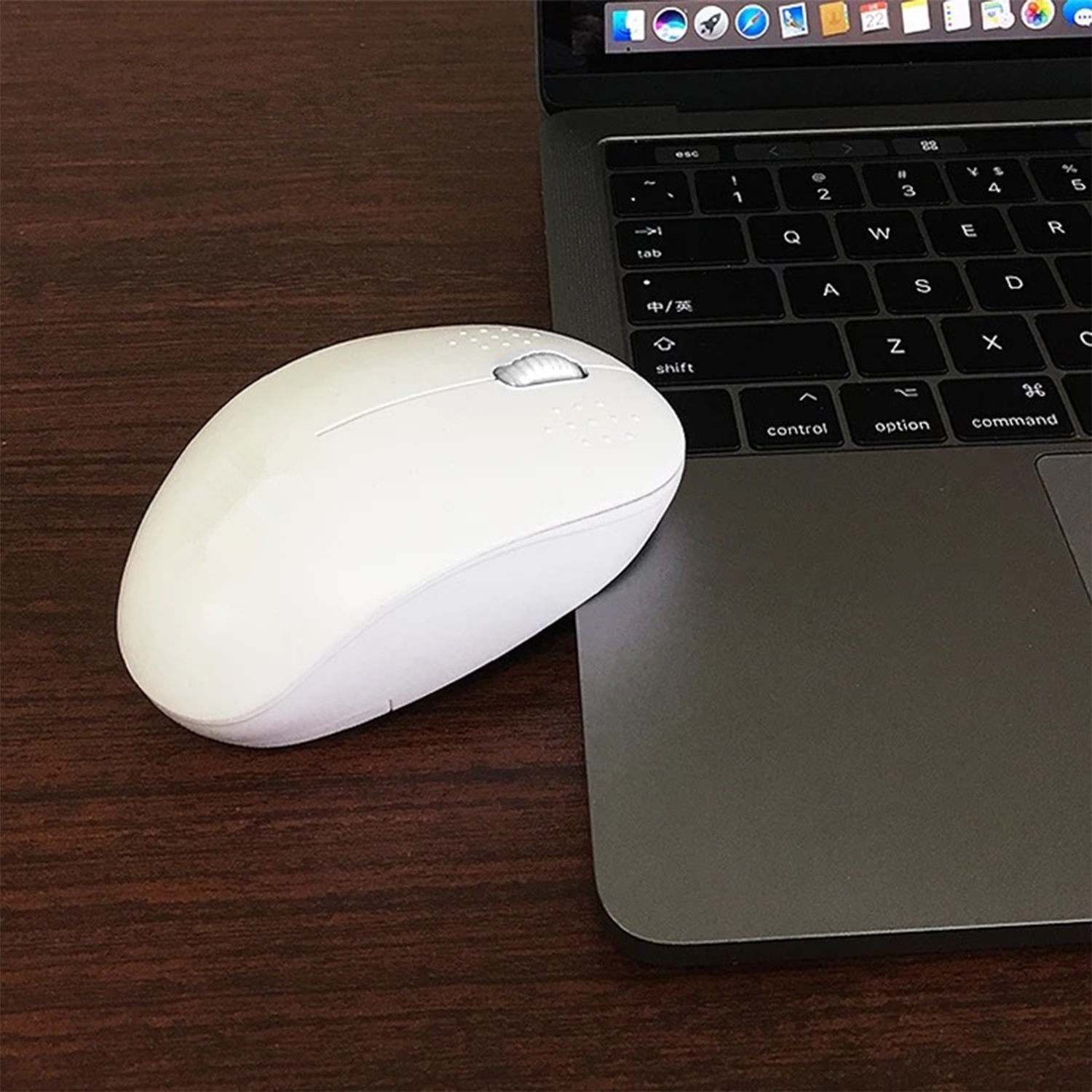 Mouse wireless bianco accanto a un laptop. Mouse su scrivania in legno. Laptop a destra.