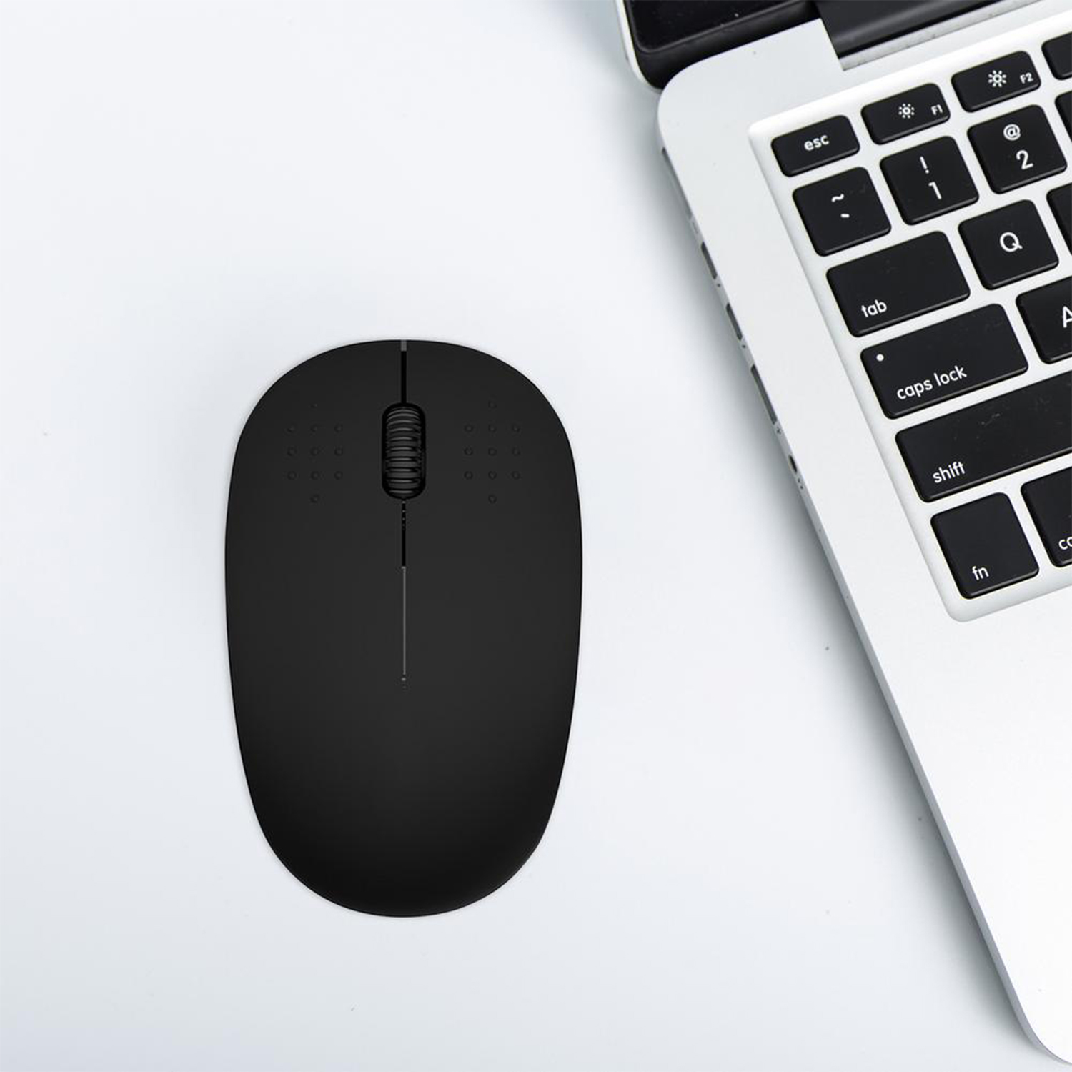 Mouse wireless nero su una scrivania bianca vicino a una tastiera per laptop.