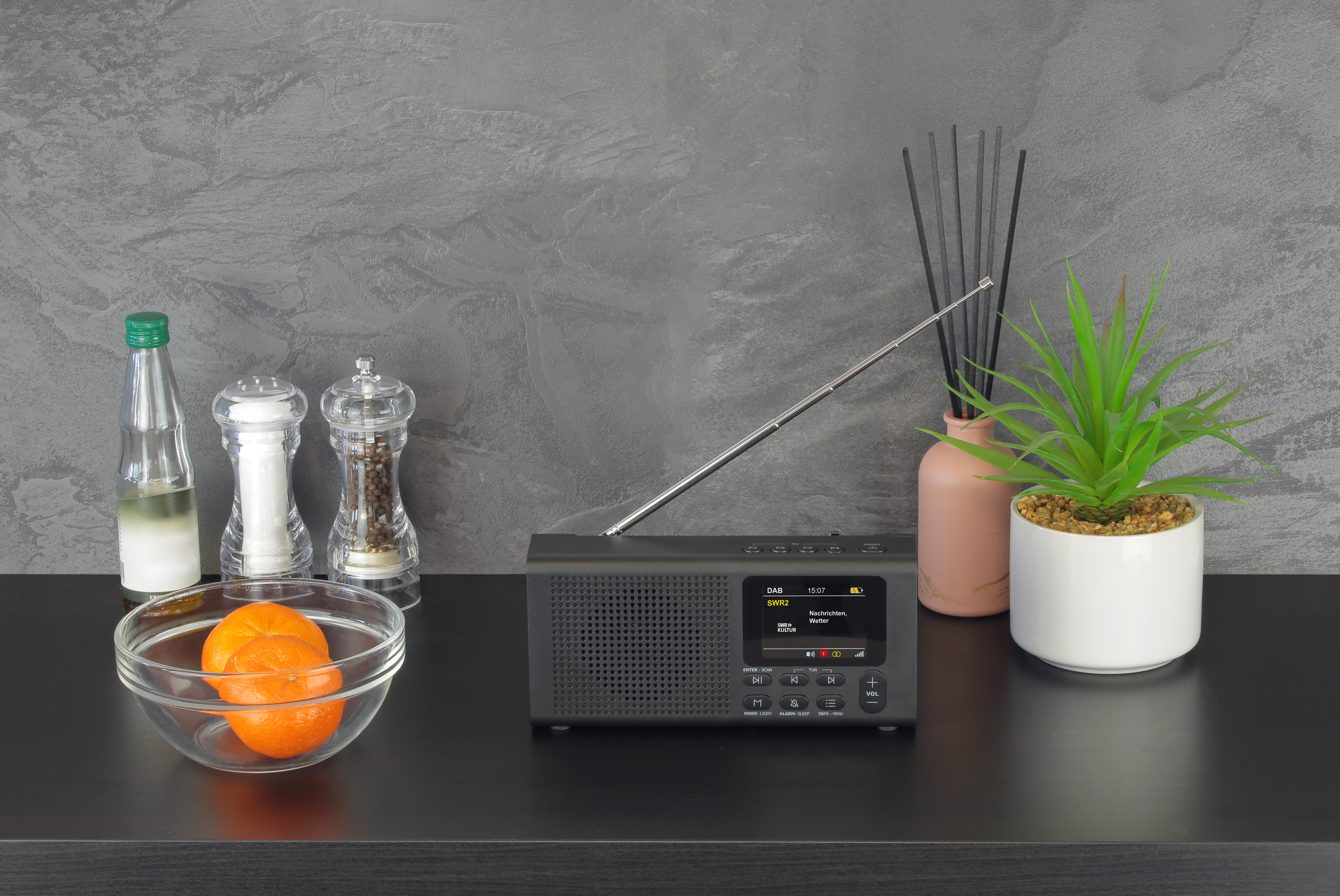 Schwarzes Radio mit Display, Glasschale mit Orange, auf Regal.