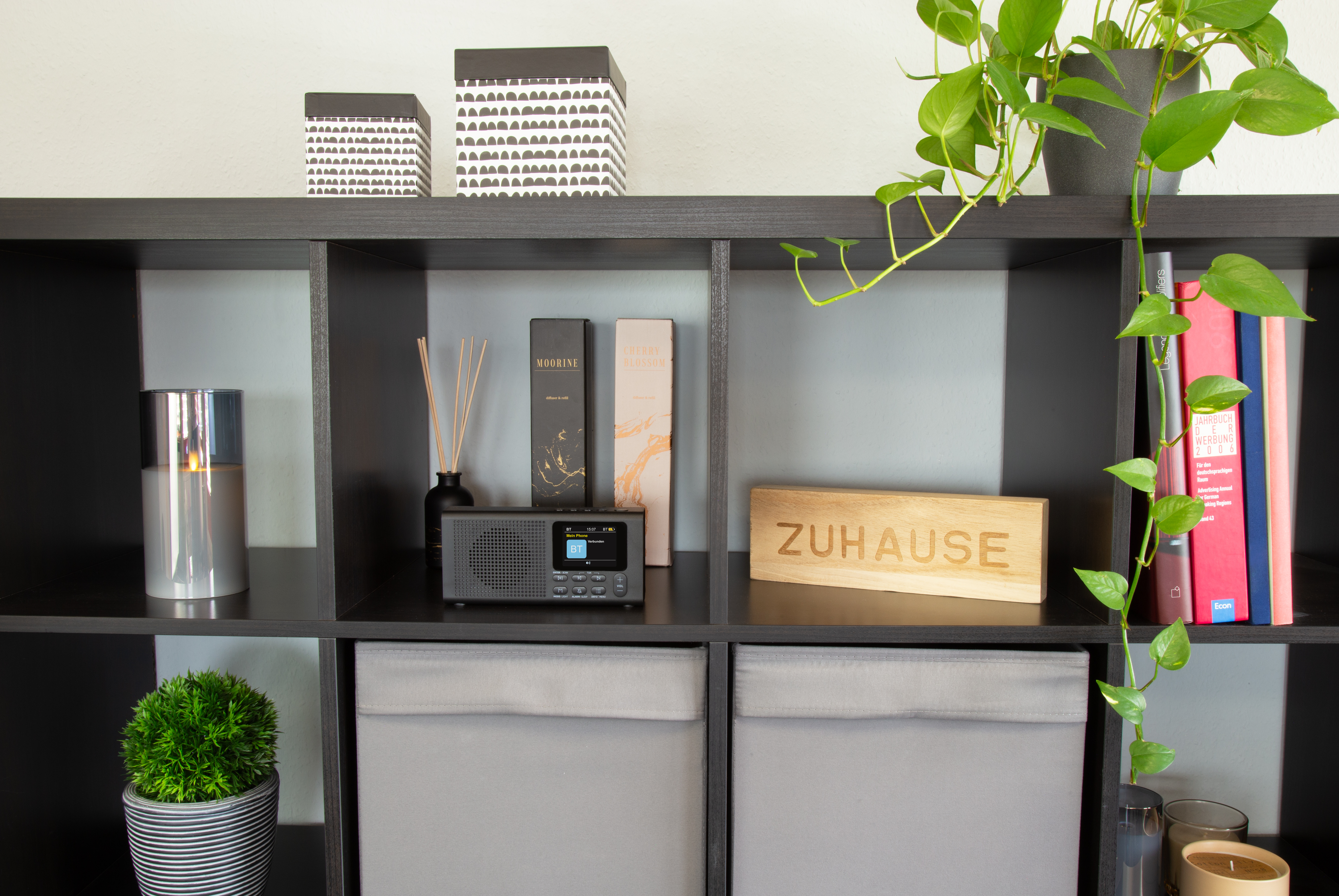 Schwarzes Regal mit Dekoartikeln, Büchern und einem Radio mit der Aufschrift 'ZUHAUSE'.