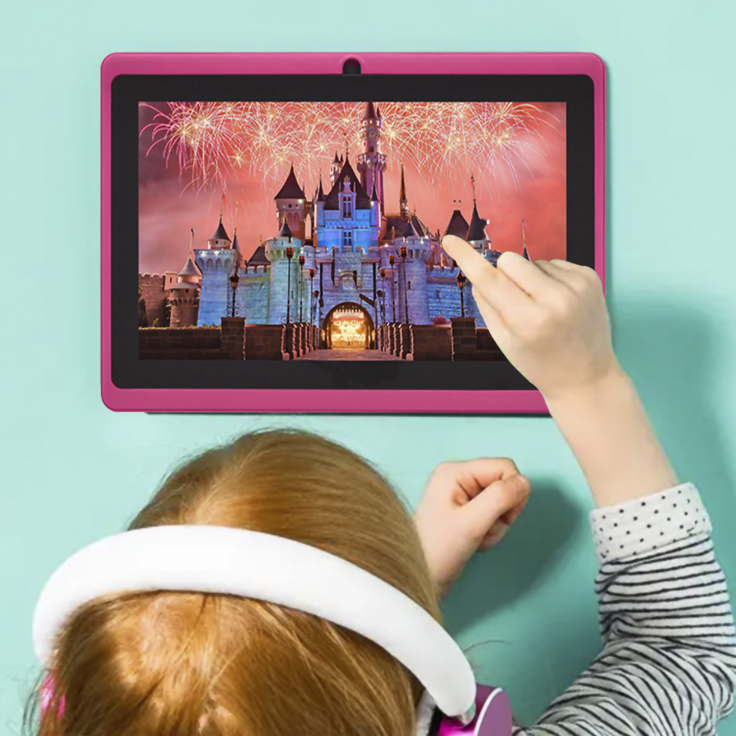 Ein Kind berührt ein Tablet, das ein Schloss mit Feuerwerk zeigt. Das Kind trägt Kopfhörer und ist an einer Wand.