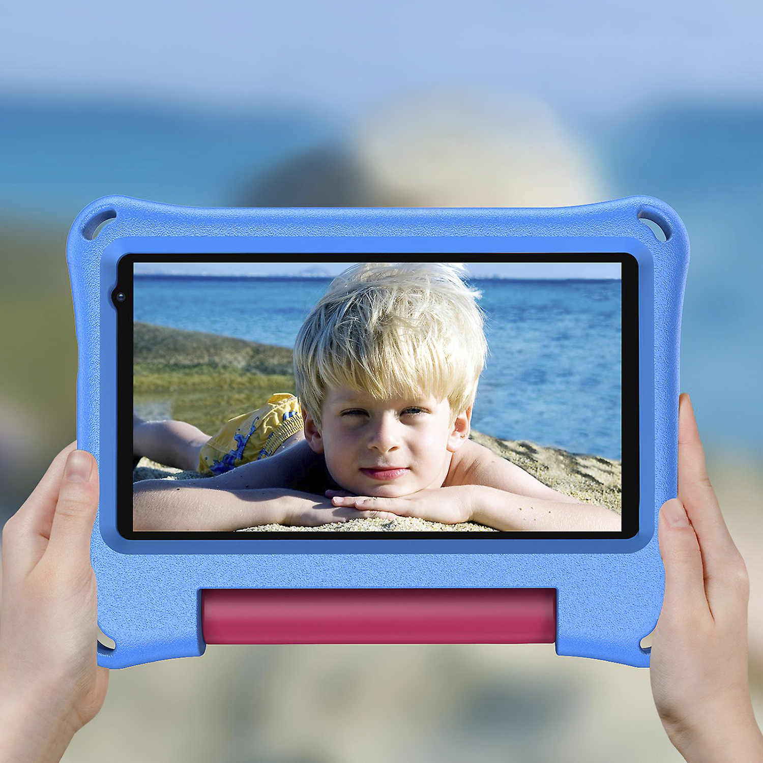 Un bambino che tiene un tablet in una custodia blu. Lo sfondo è una scena di spiaggia.