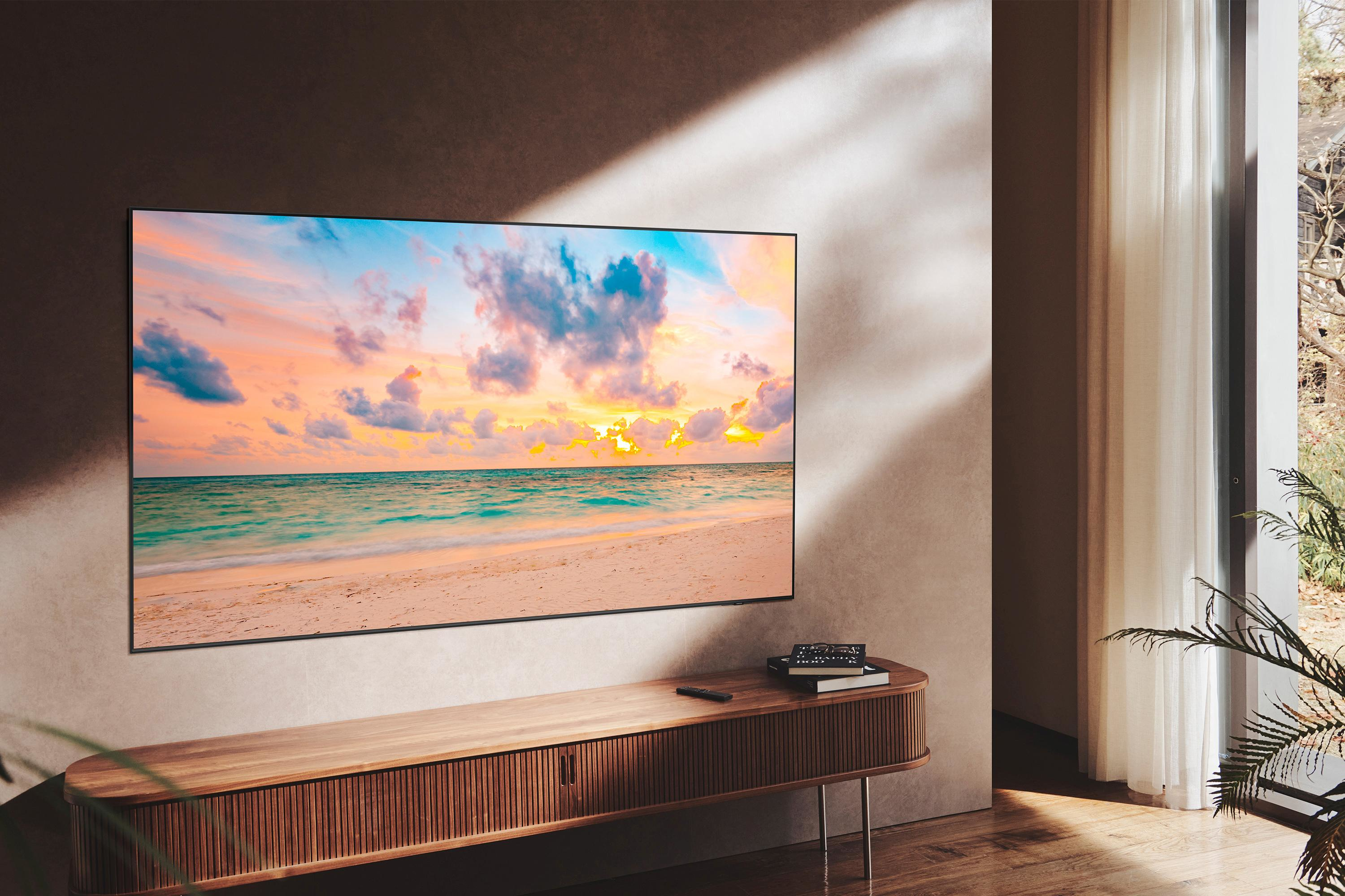 Una TV mostra una scena di spiaggia con un tramonto, su un mobile in legno in una stanza con parete beige.