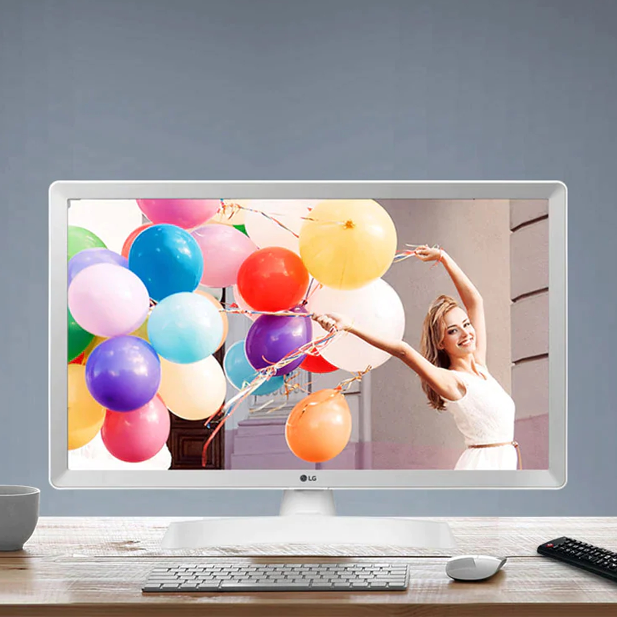 Un monitor LG bianco mostra una donna che tiene dei palloncini. Sono visibili un mouse bianco e un telecomando.