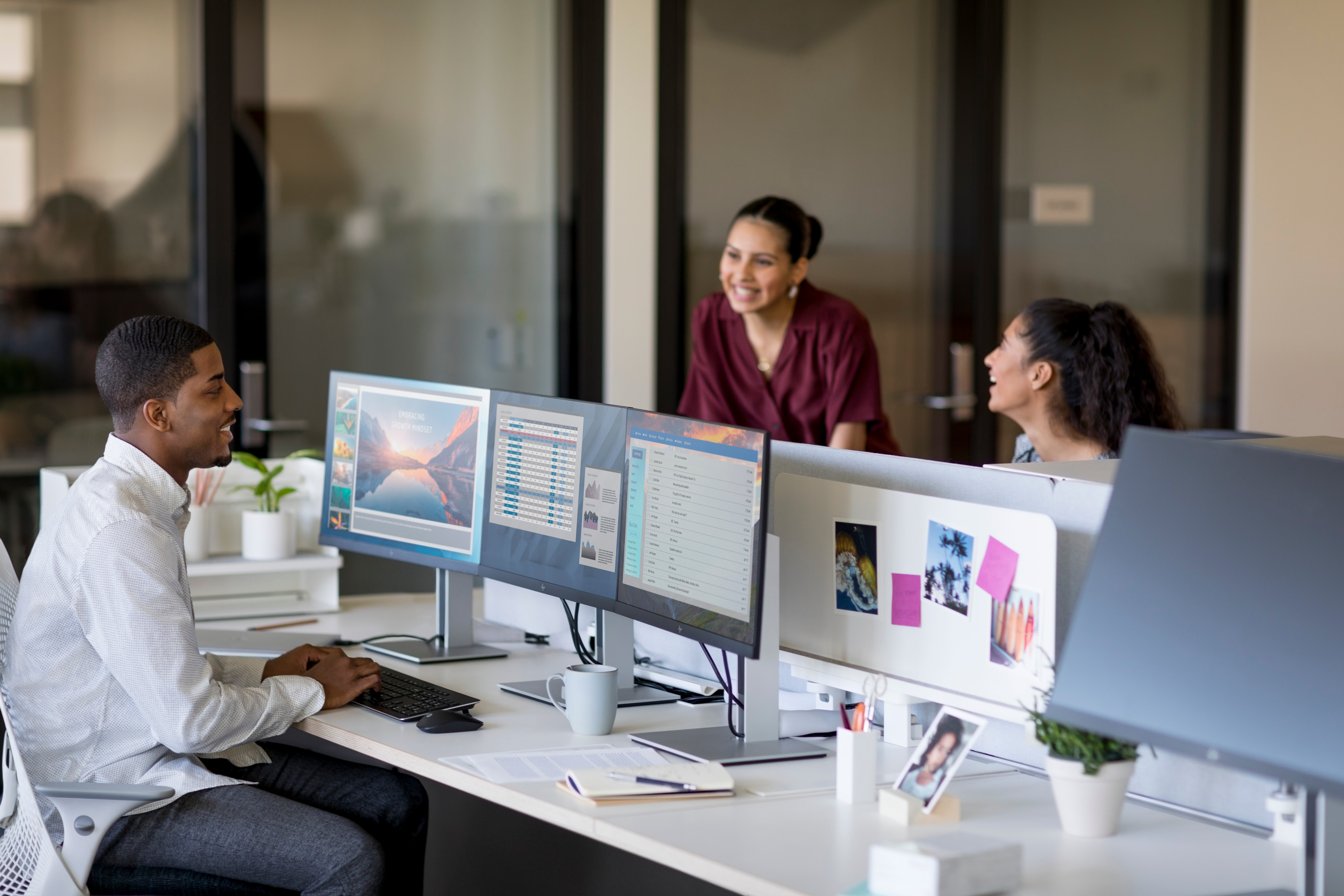 Three people in an office setting work at computers. Monitors display data and graphics.