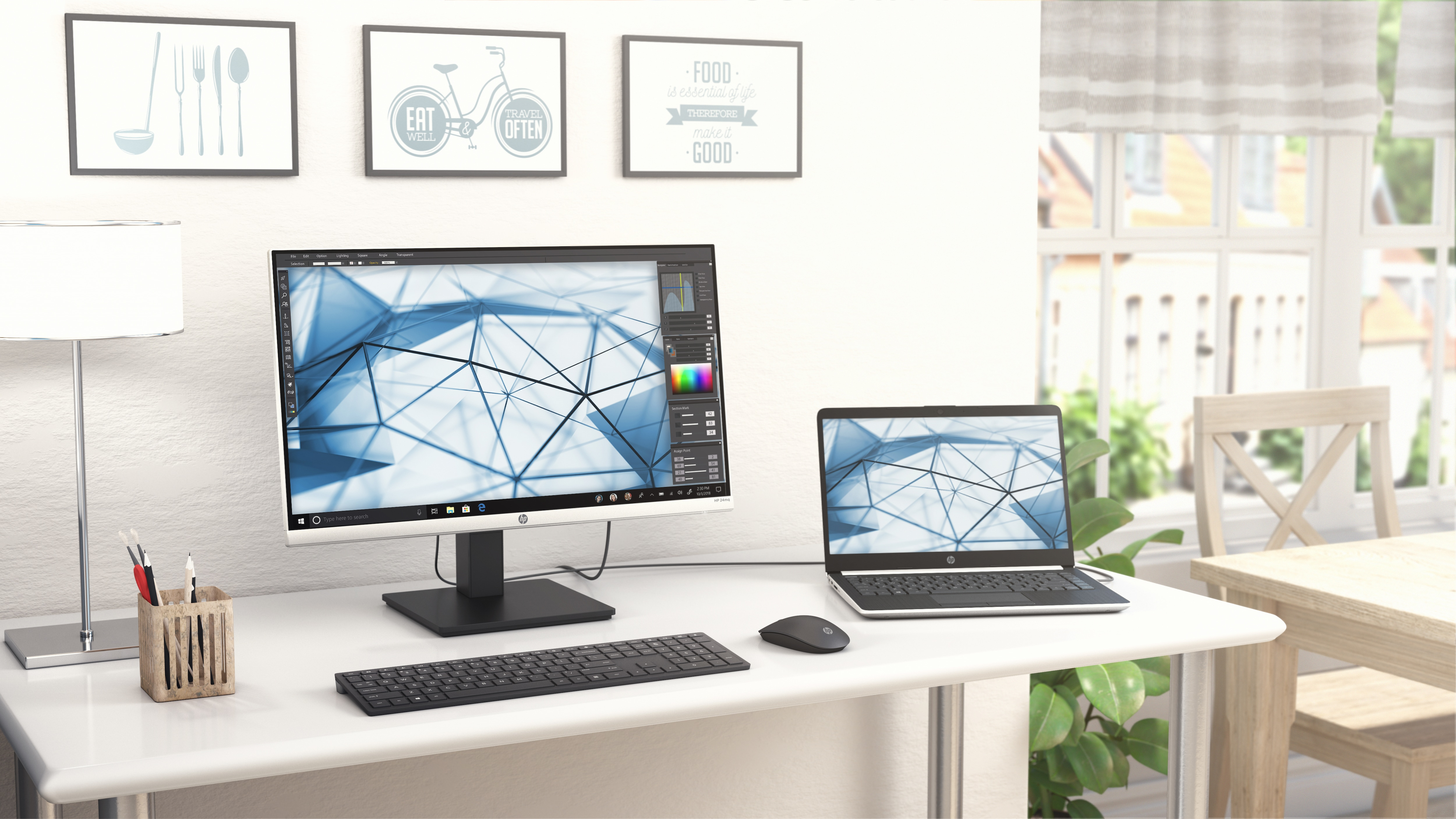 Una scrivania con monitor, laptop, tastiera, mouse e quadri con cornice.