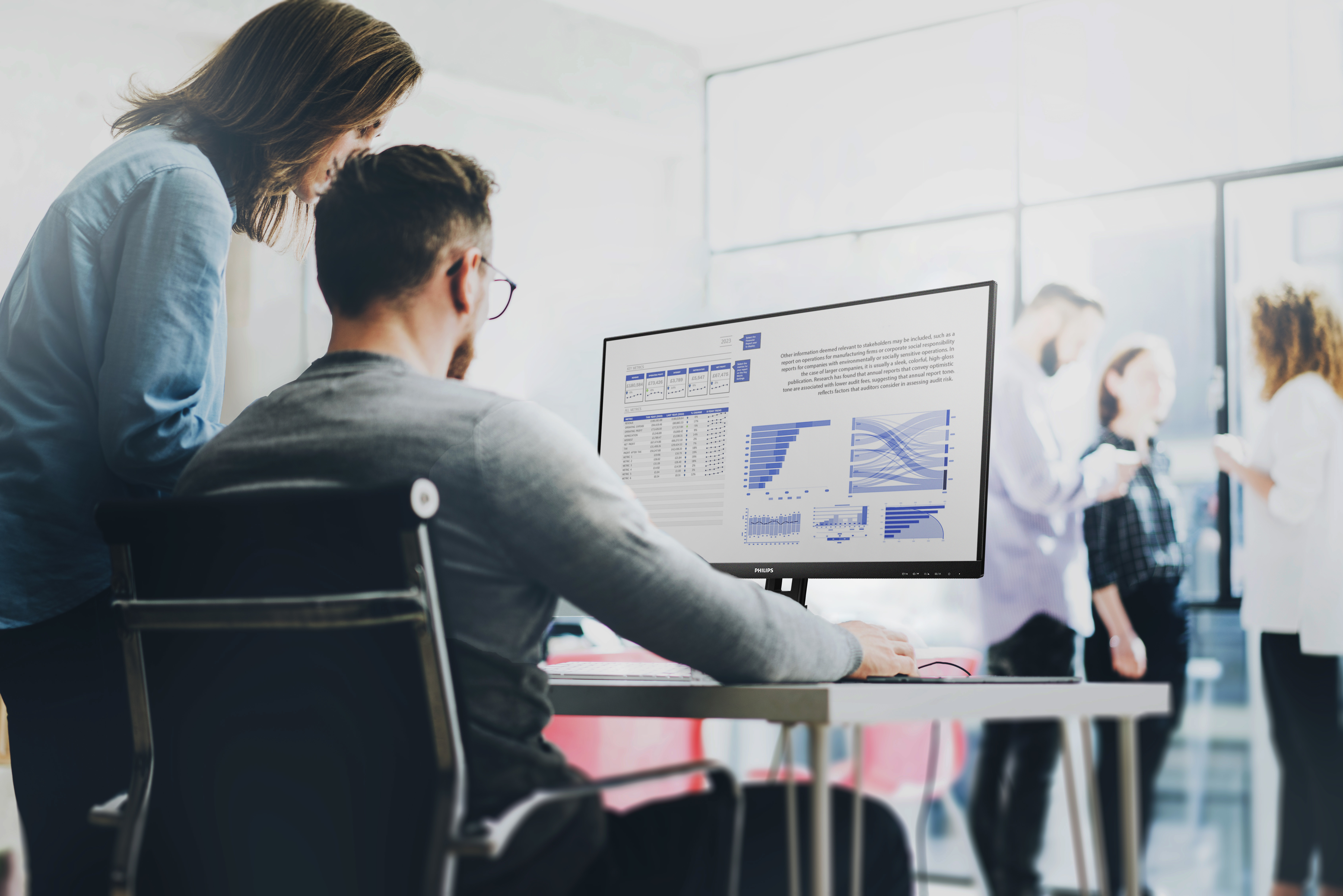 Ludzie w biurze, patrzący na ekran komputera z wykresami danych, wykresami i liczbami.