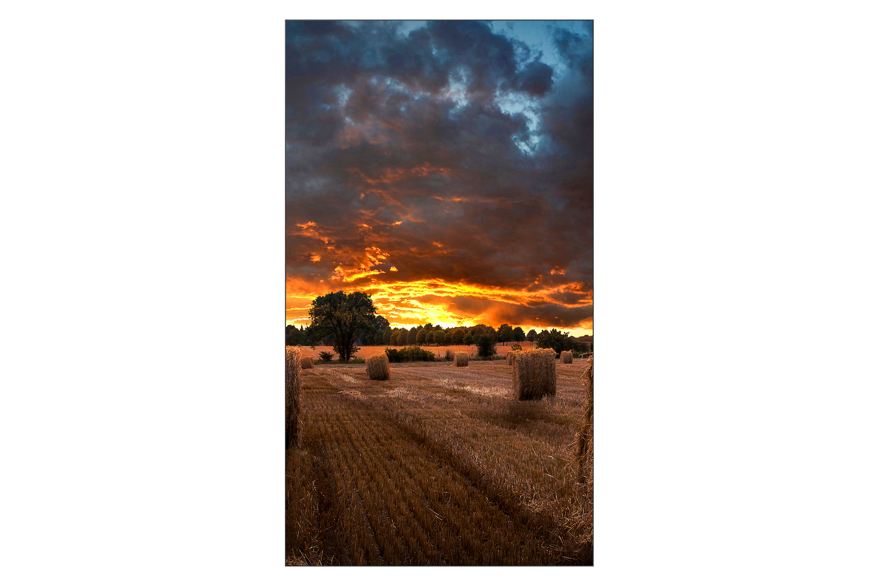 Ein Feld mit Heuballen und Sonnenuntergang mit dunklen Wolken und orangem Himmel.