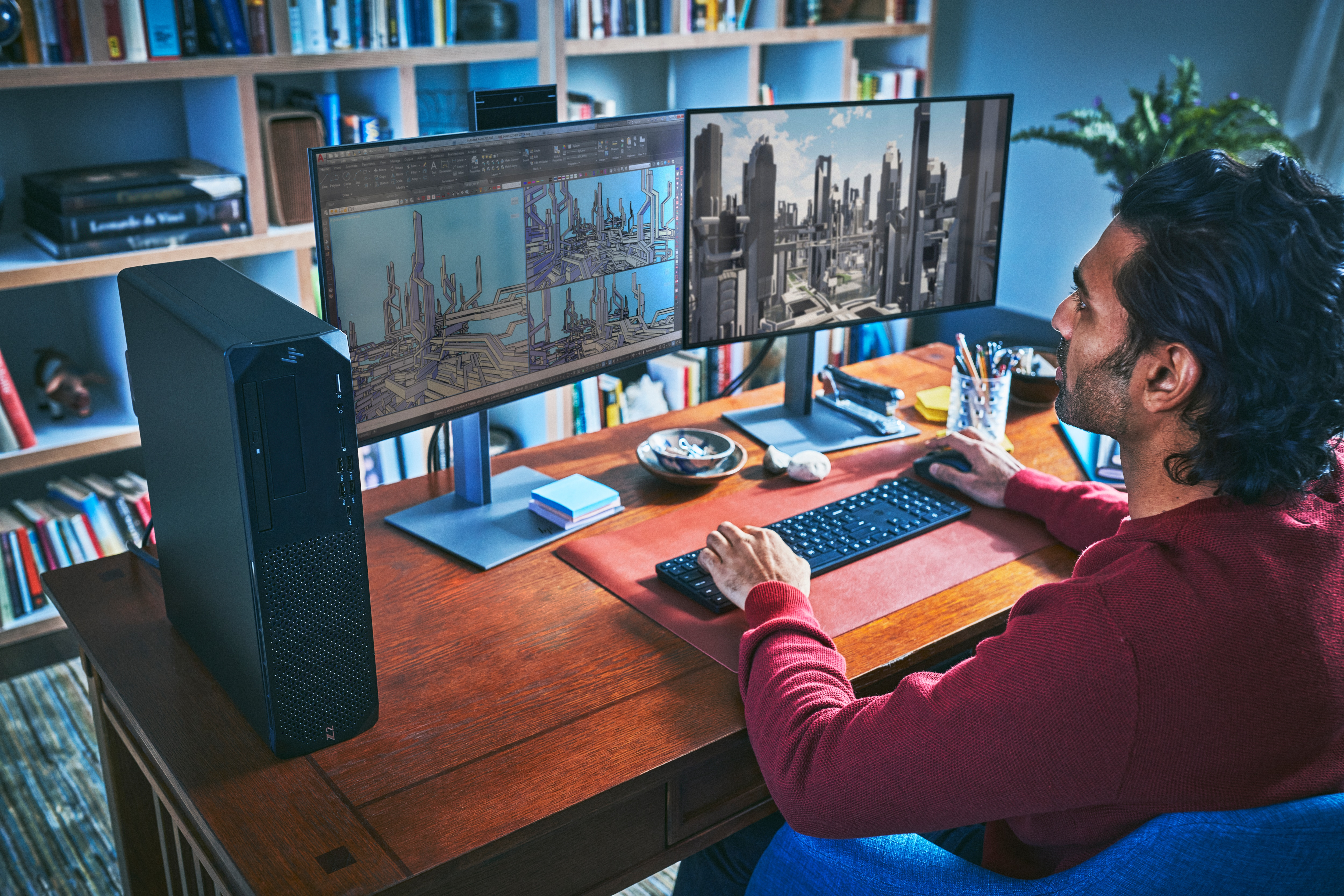 Mężczyzna pracuje przy biurku z dwoma monitorami i komputerem. Tło to regał z książkami.