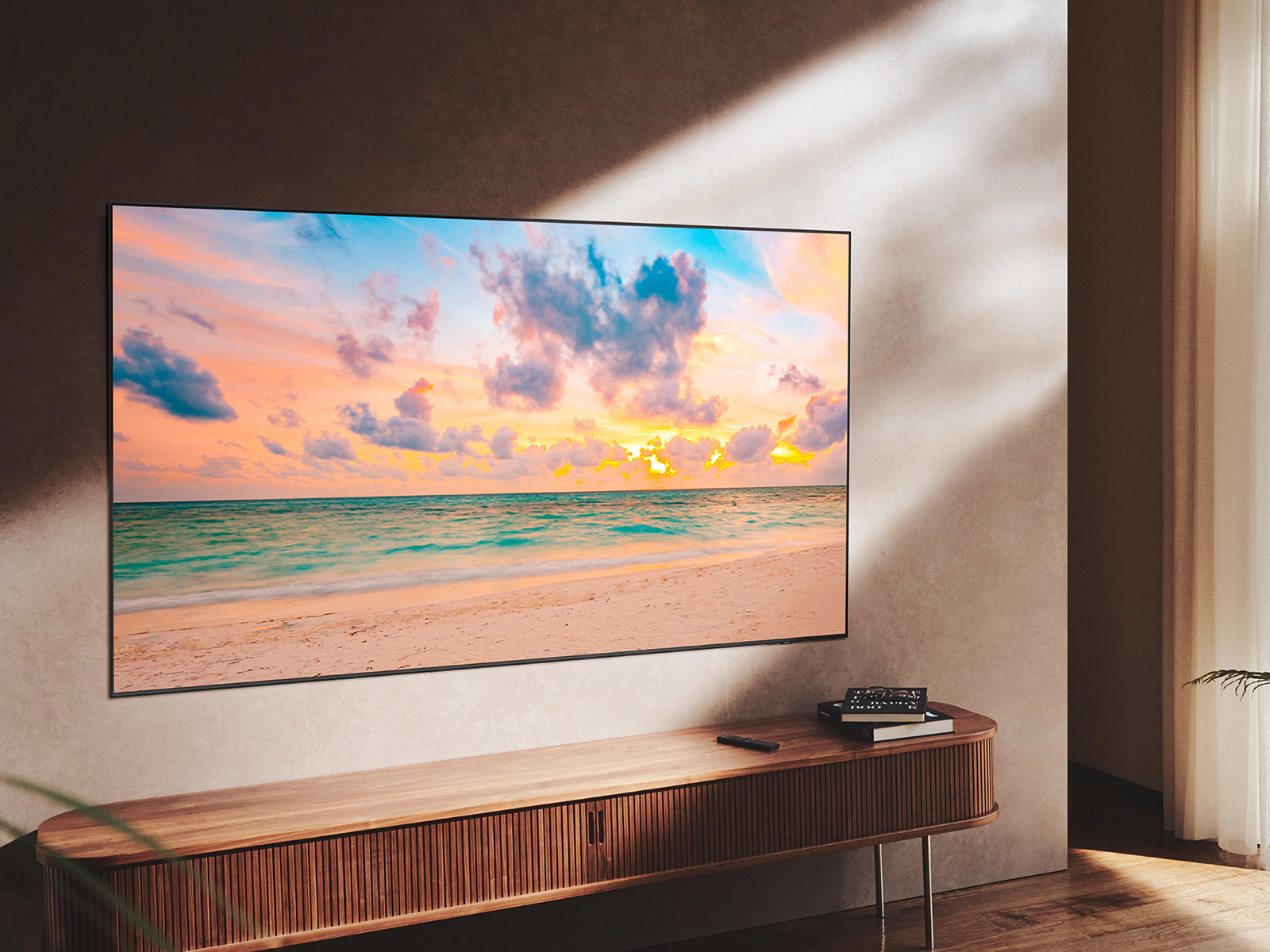 Ein großer Fernseher an der Wand, zeigt eine Strandszene bei Sonnenuntergang, mit Holzschrank.