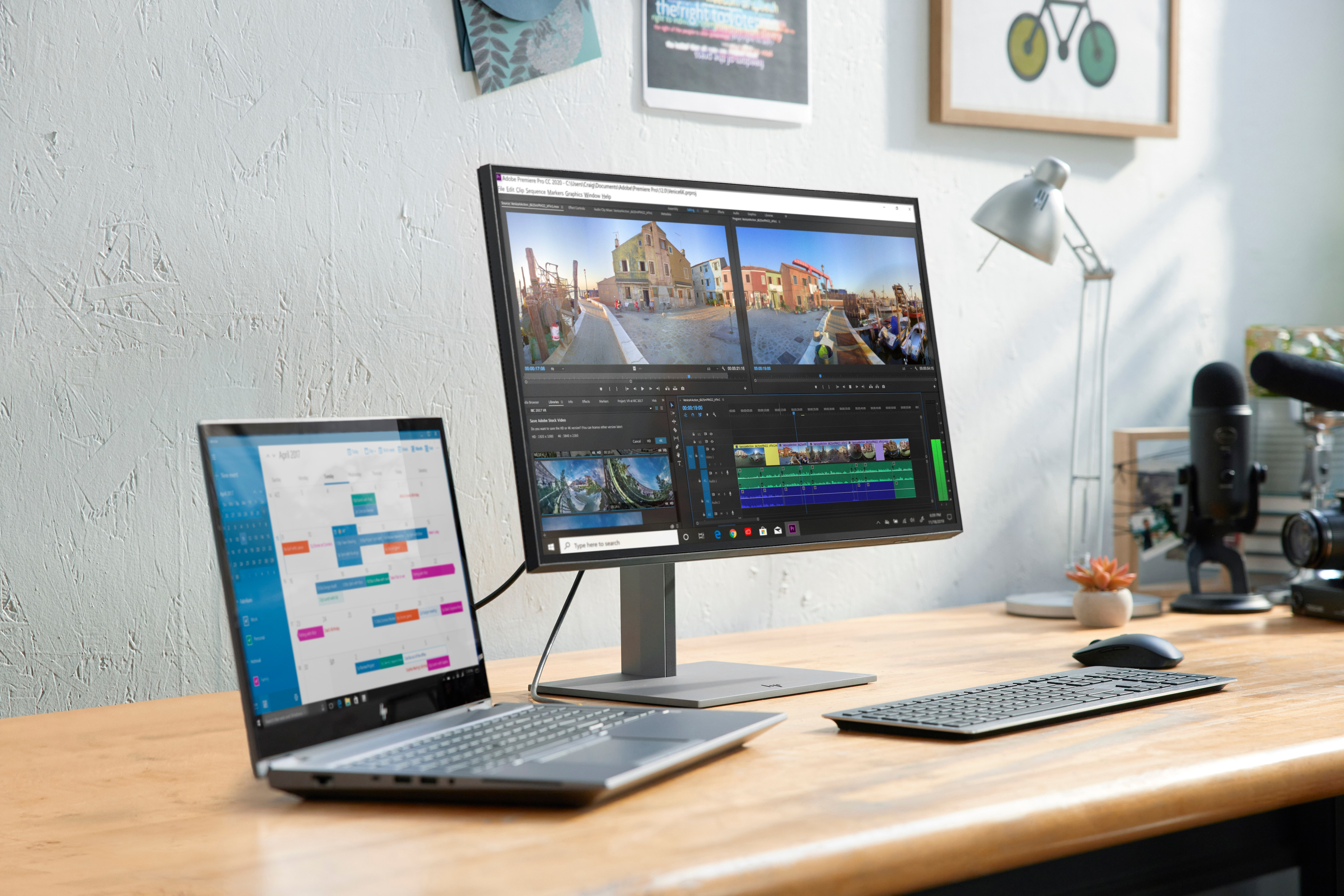 Ein Schreibtisch mit Laptop und Monitor. Der Monitor zeigt eine Videobearbeitungssoftware. Ein Mikrofon und eine Tastatur sind sichtbar.